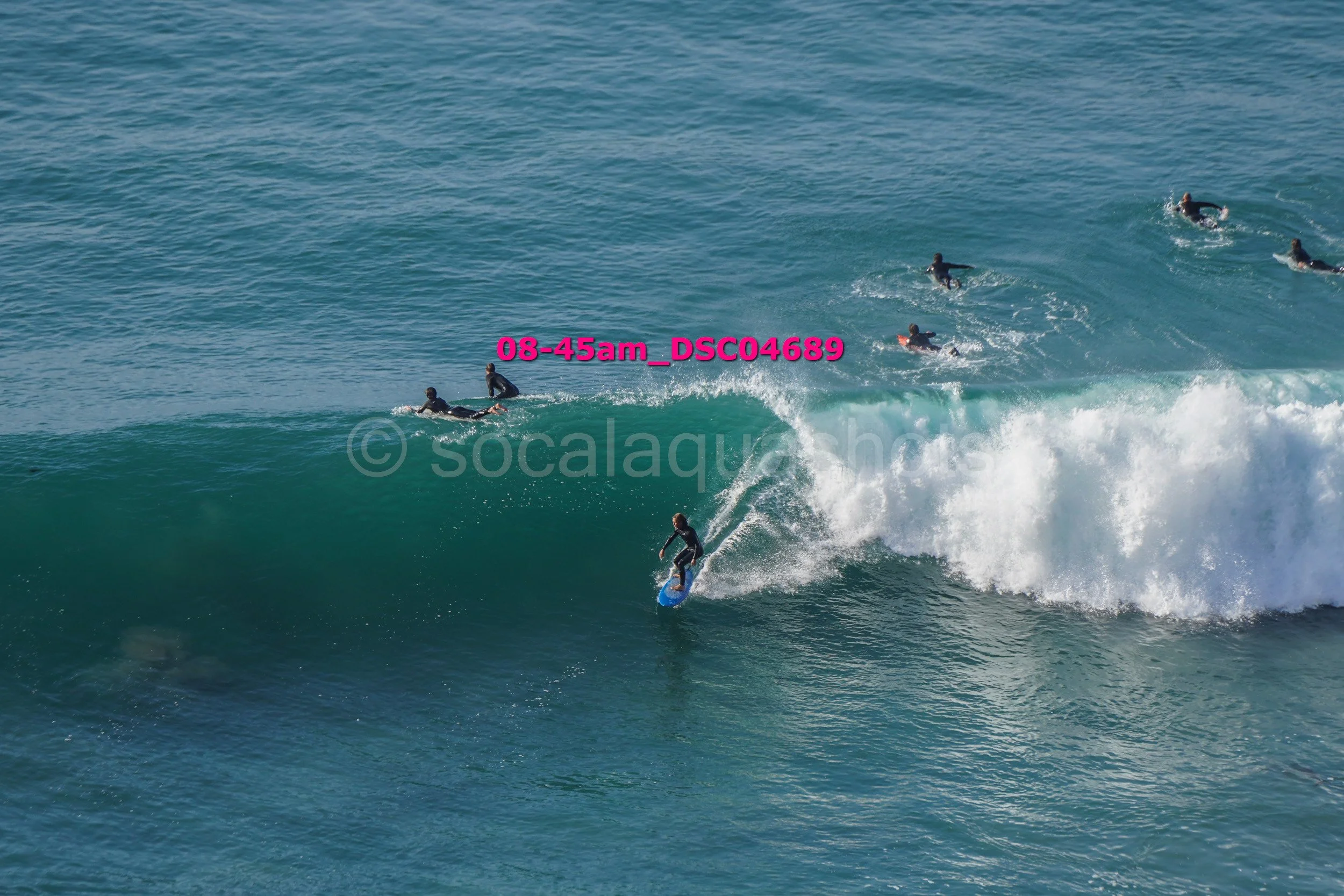 Surfer riding a wave with multiple surfers on the water behind him.