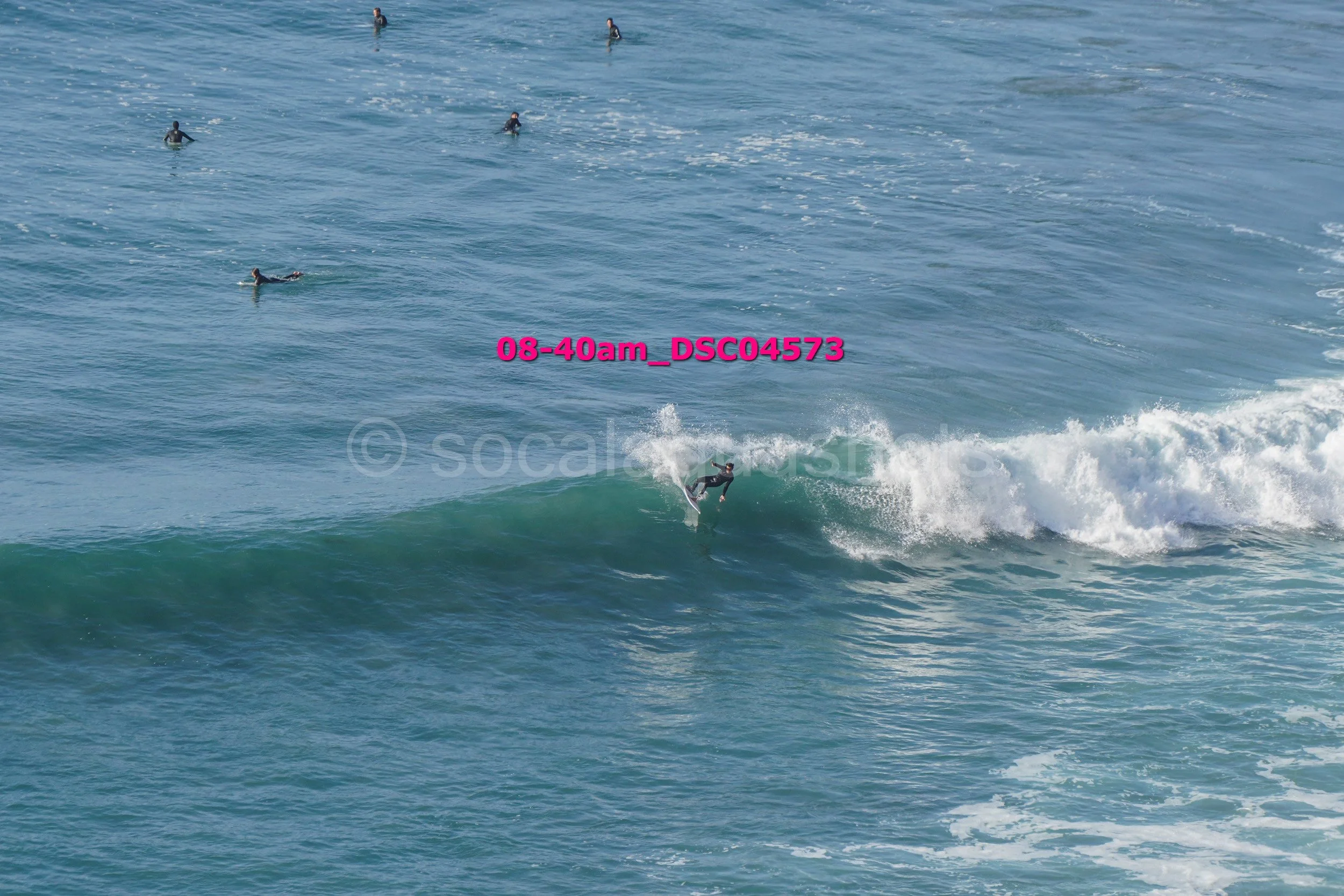 A person surfing on a wave in the ocean with several other surfers floating in the water nearby.