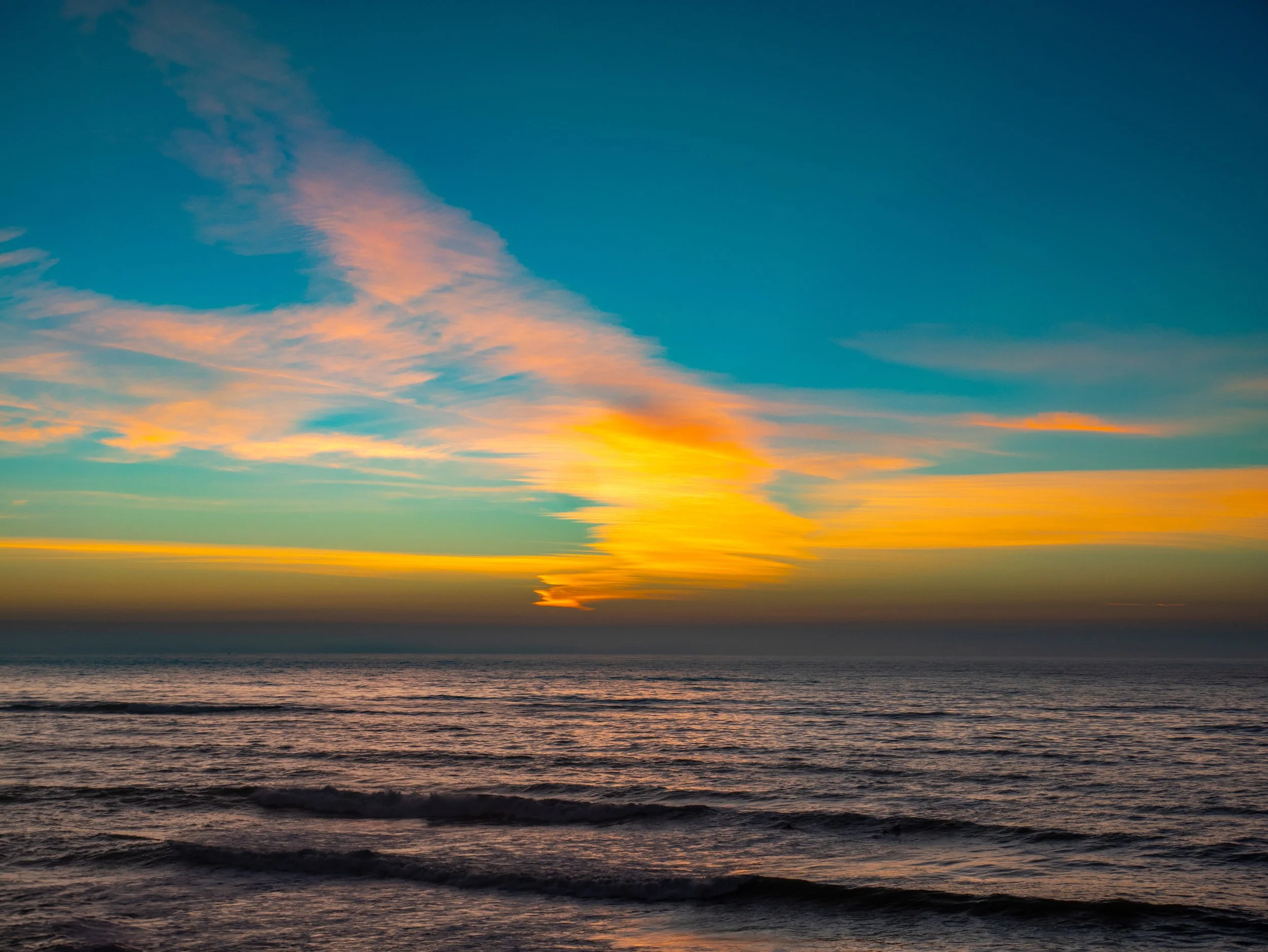 Colorful sunset over the ocean with calm waves and a partly cloudy sky.