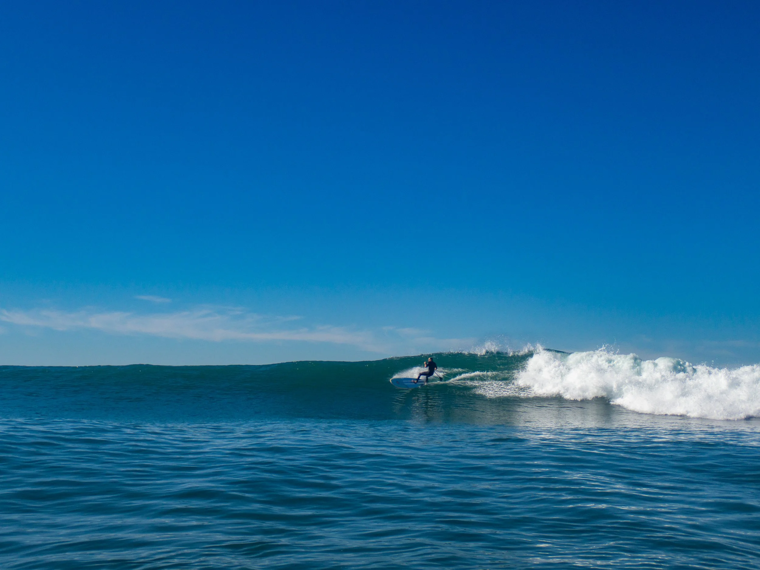 A person surfing on a wave in the ocean under a clear blue sky.