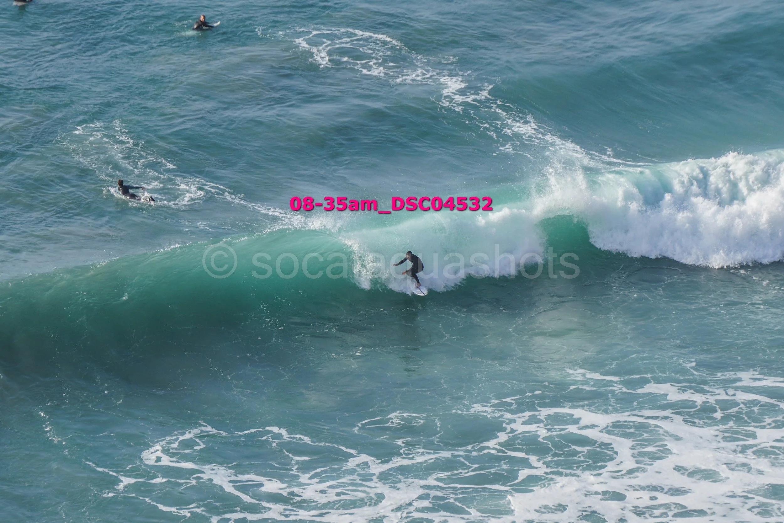 Surfer riding a wave with two other surfers in the water during the daytime.