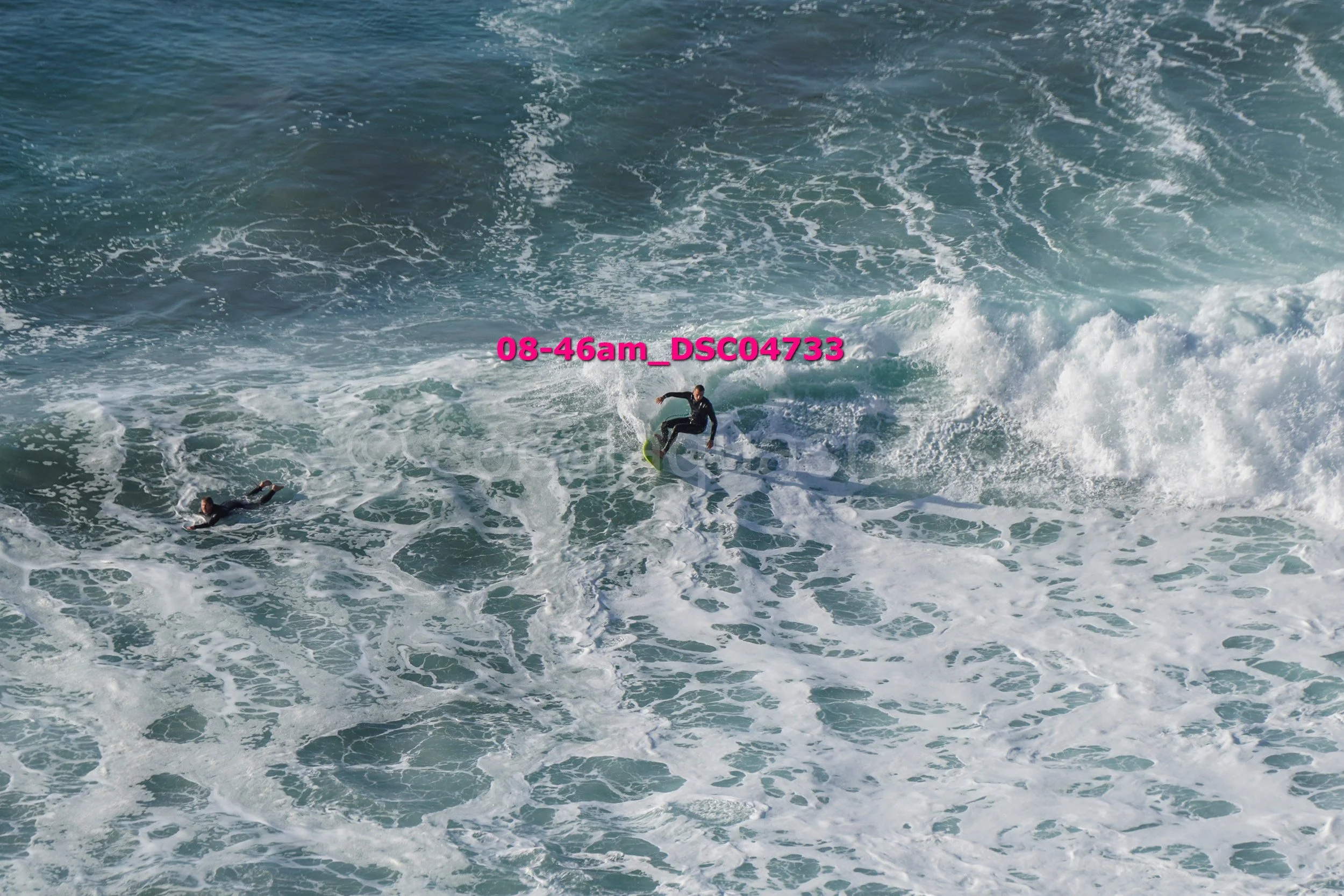 A person surfing on a wave in the ocean, with another person swimming nearby.