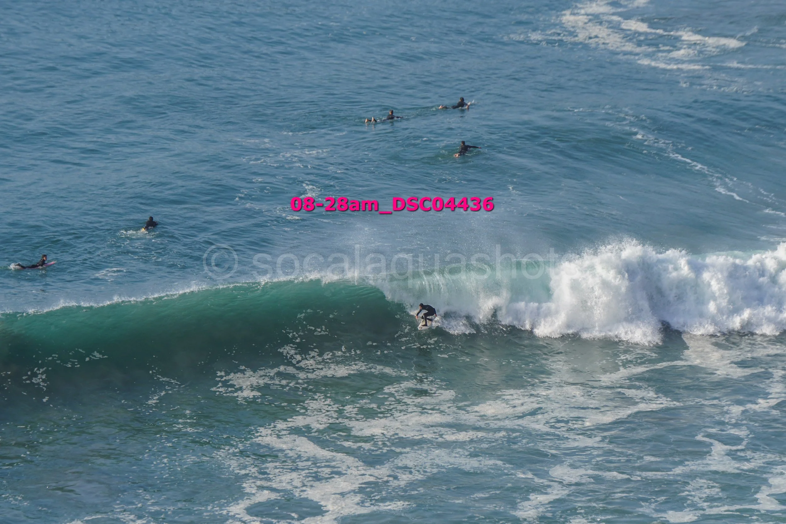 Surfer riding a wave with several other surfers in the water behind him