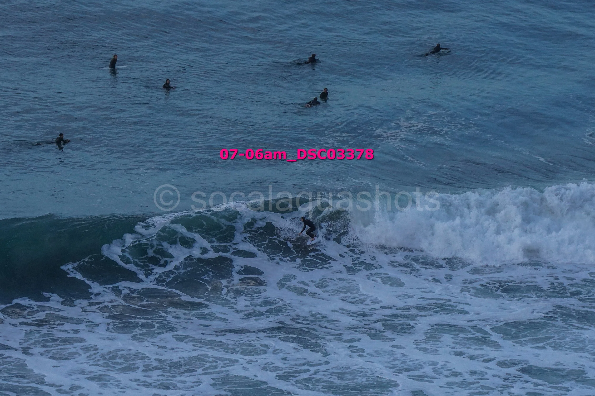 A person surfing on a wave with several people in the water in the background during daylight.