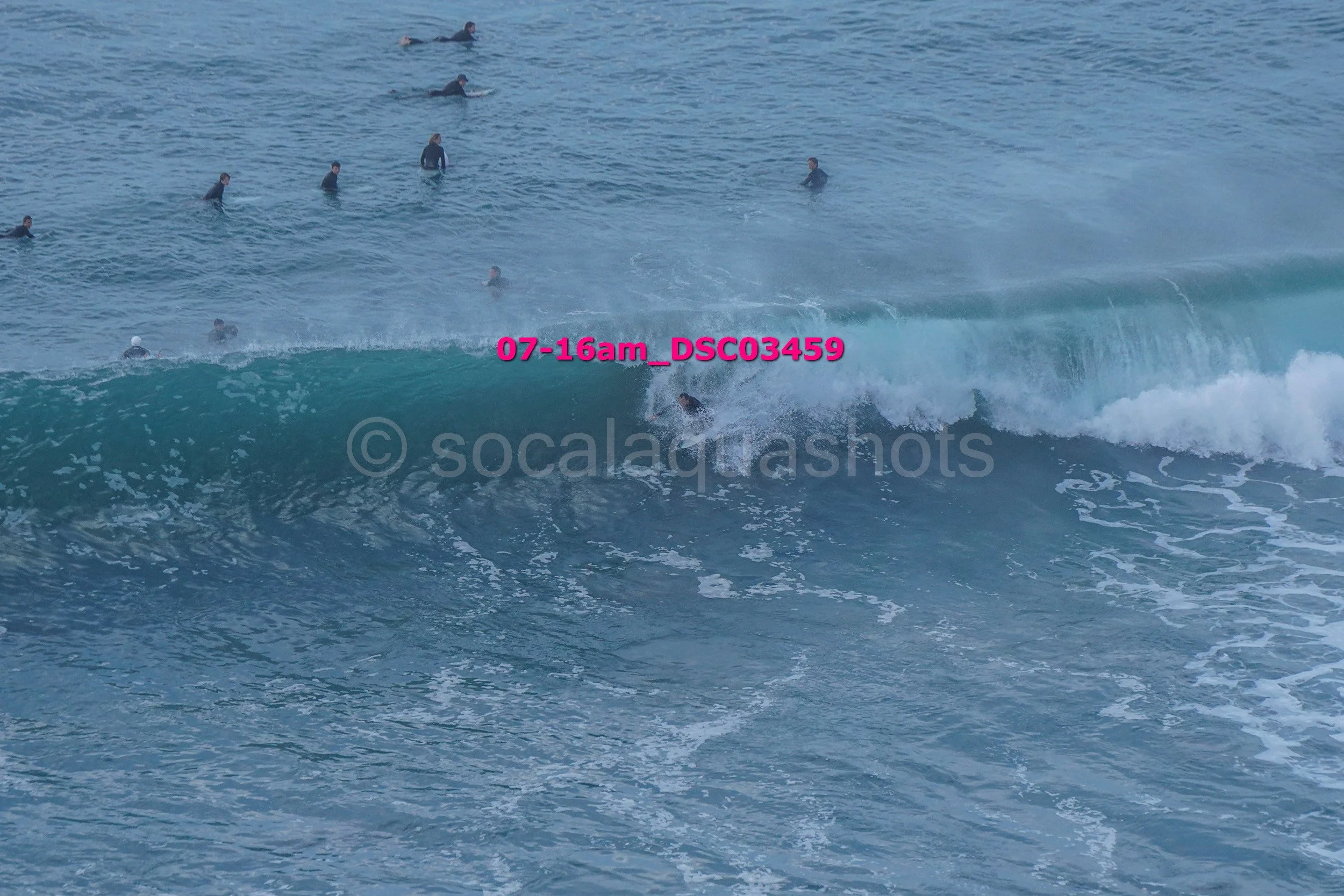 People surfing in the ocean with waves, some waiting on surfboards and others riding a wave.