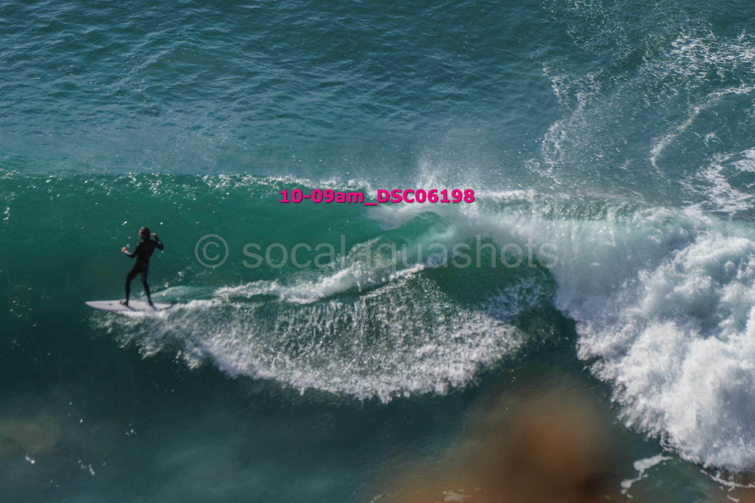 A person surfing on a large ocean wave with a water spray and bright sunlight