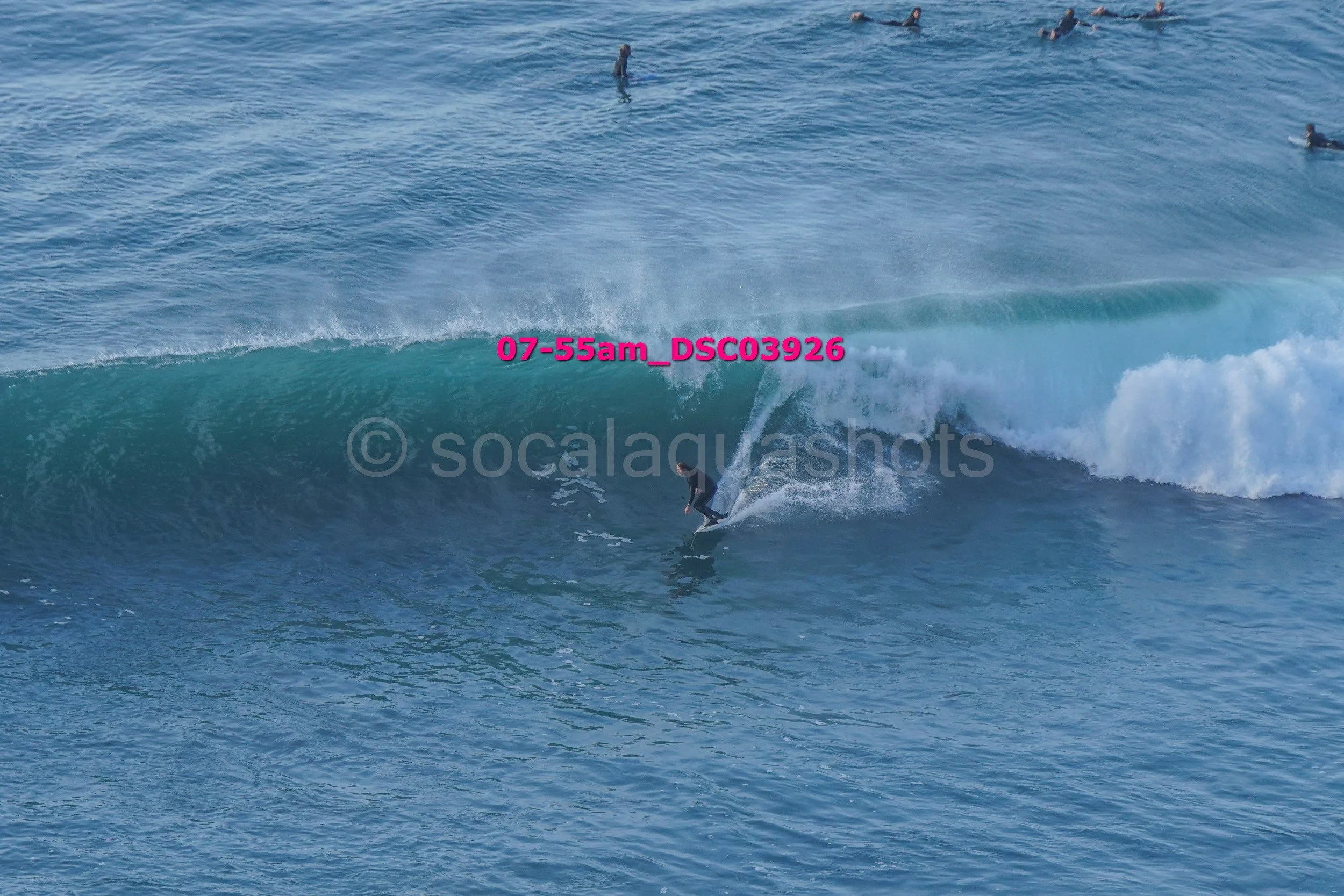 Surfer riding a large wave in the ocean with other surfers in the background.
