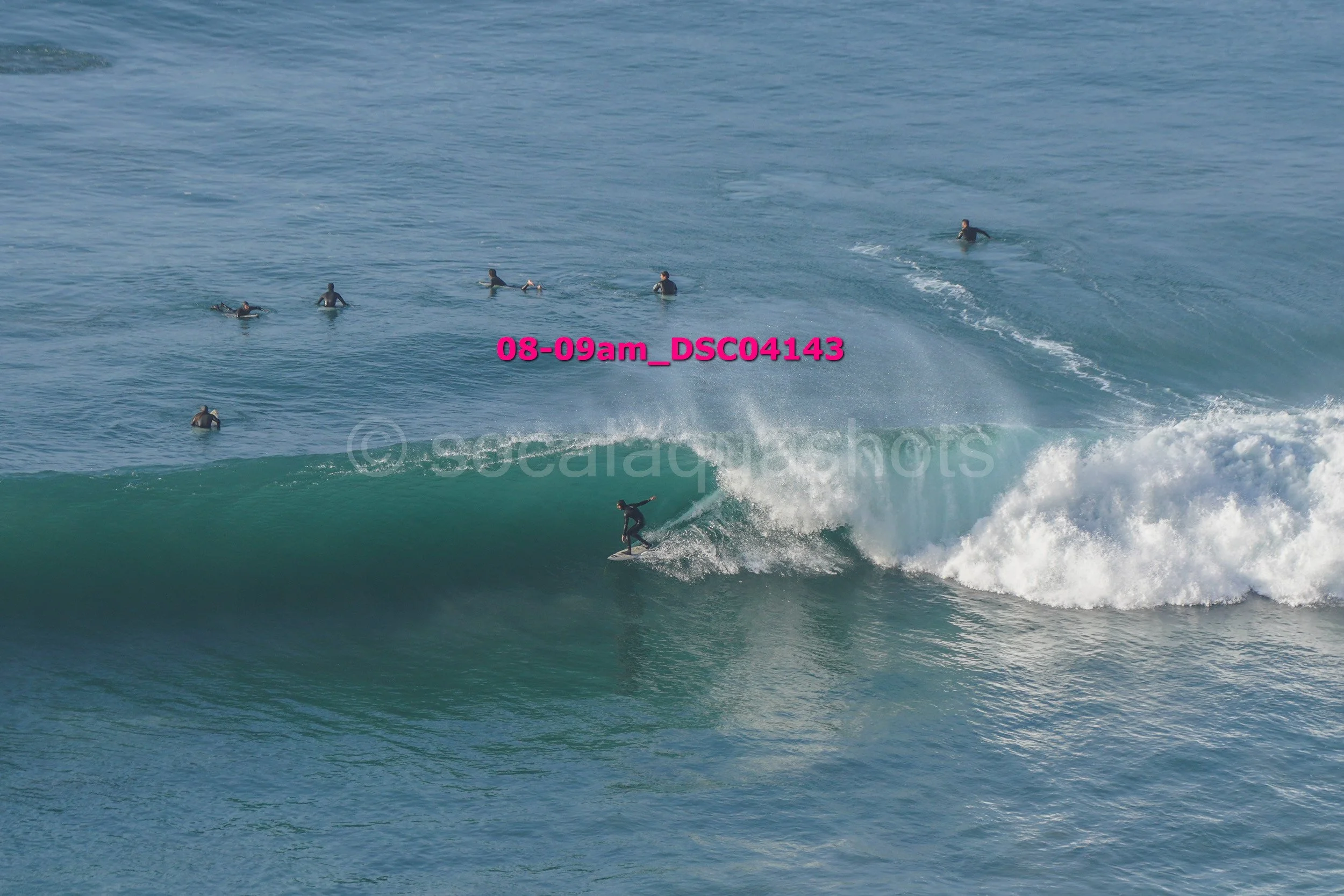 Surfer riding a wave with several people in the water watching from the background.