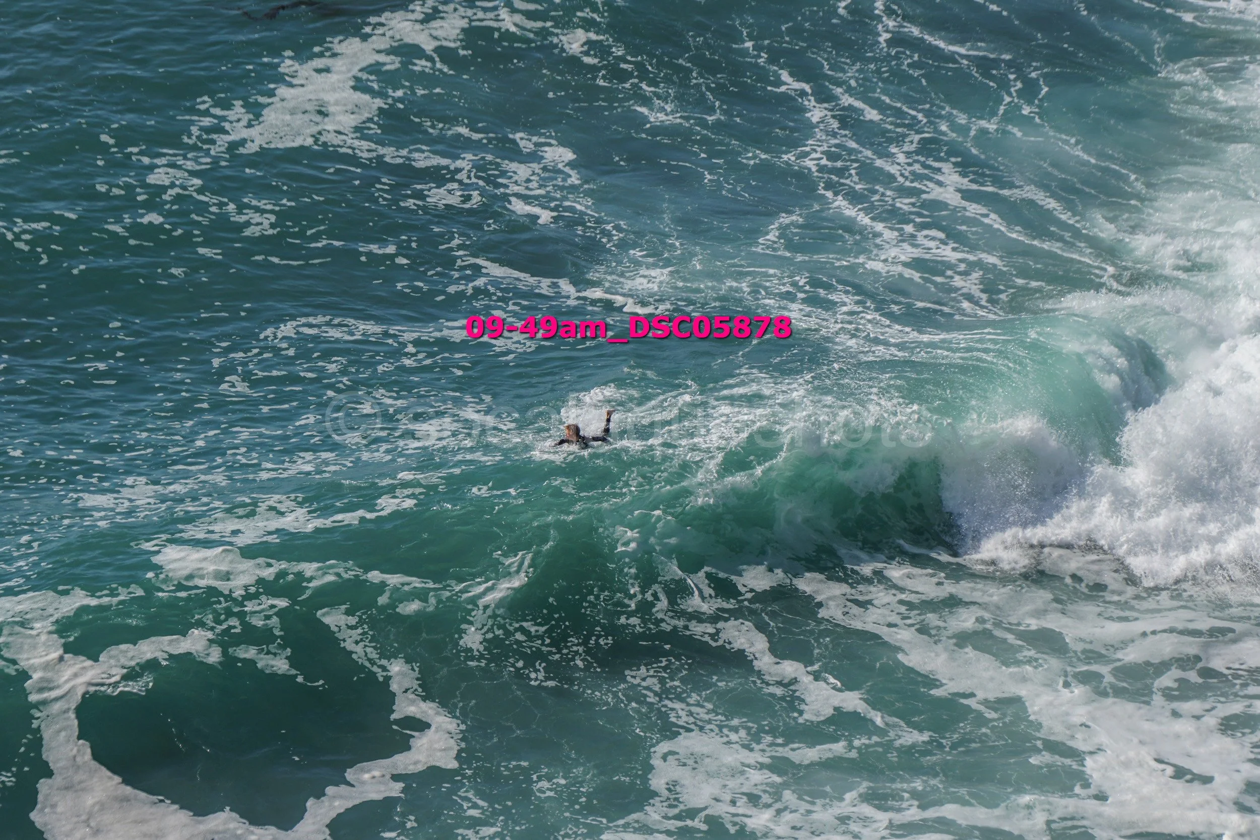 A person swimming in rough ocean water with large waves and white foam.