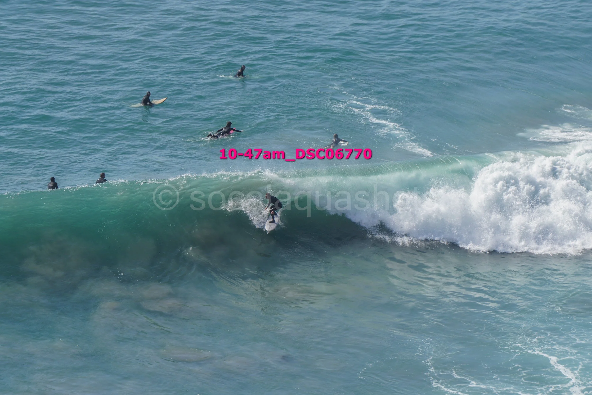 Surfer riding a wave at the beach with several people in the water watching.