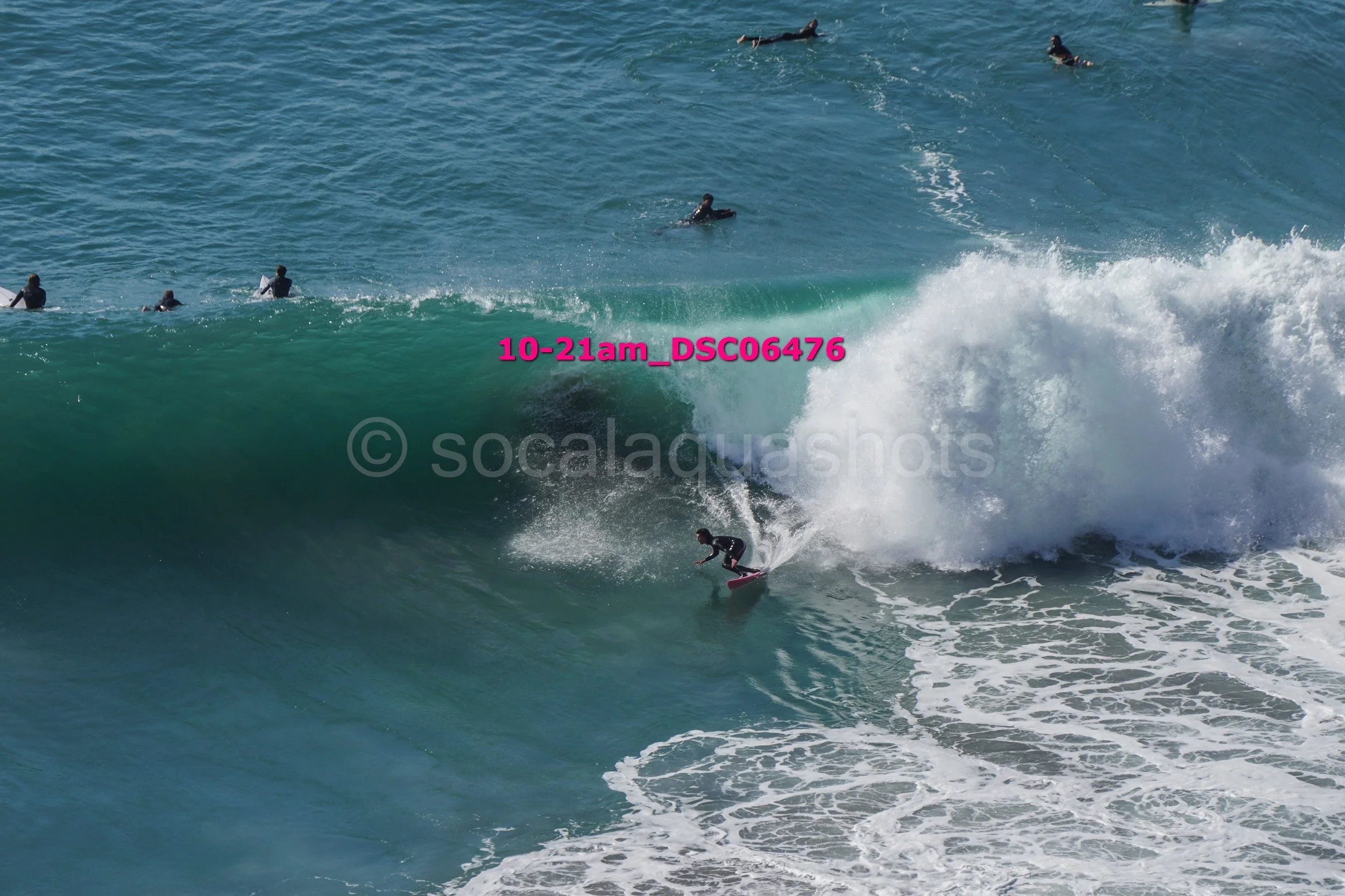 A surfer riding a large wave while several other surfers float in the water nearby