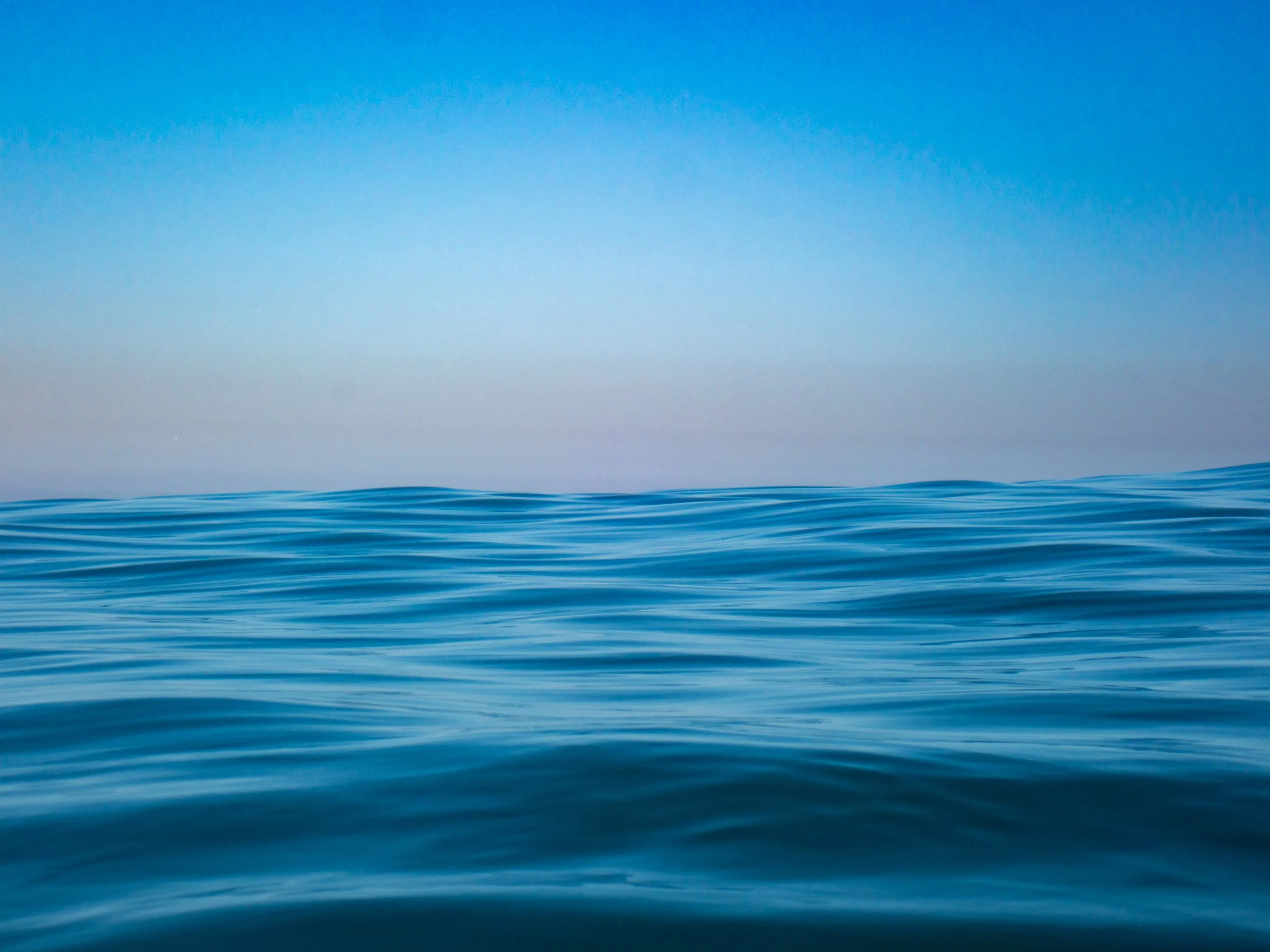 Calm ocean water with gentle waves under a clear blue sky during daytime.