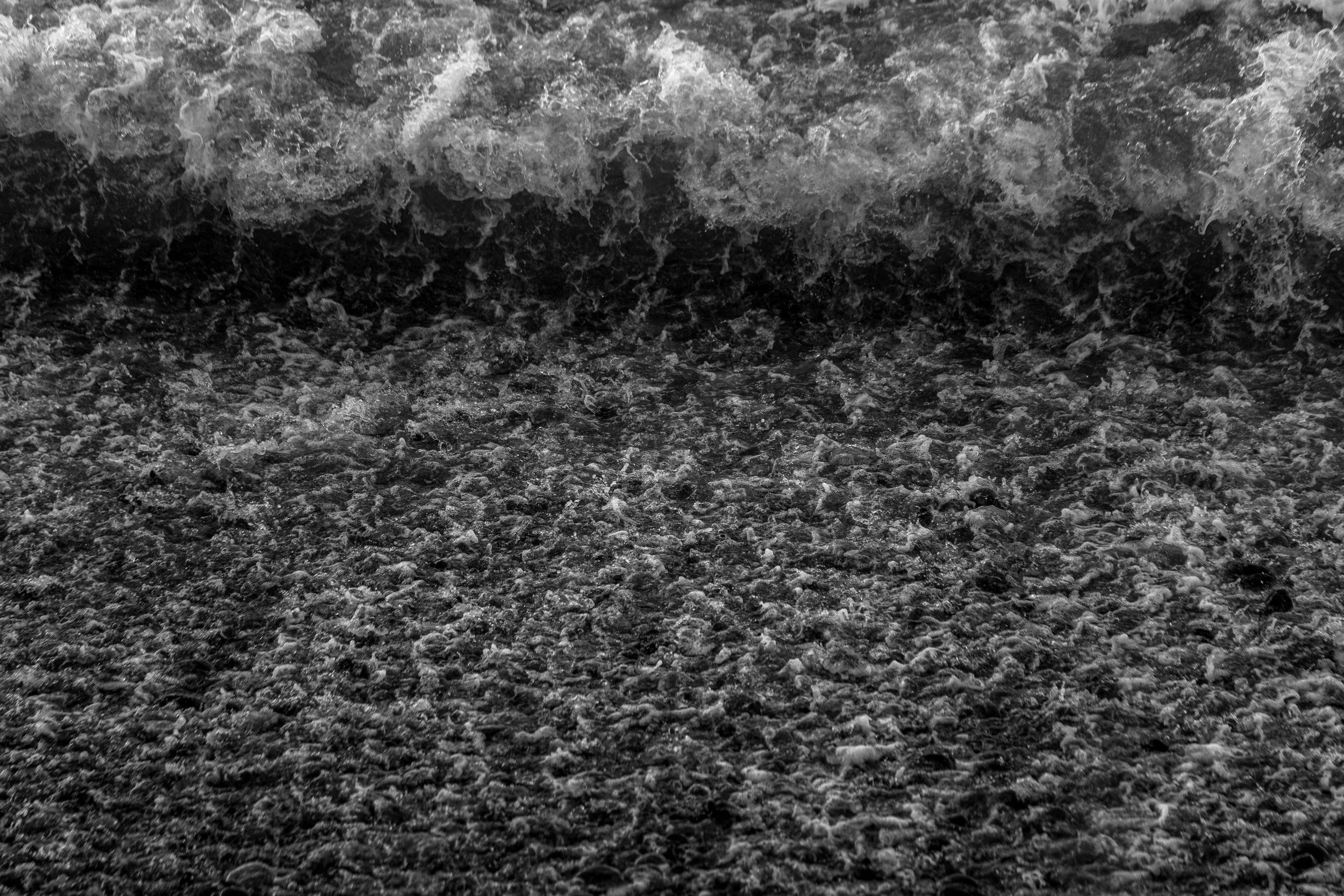 Close-up of black and white ocean waves crashing onto the shore.