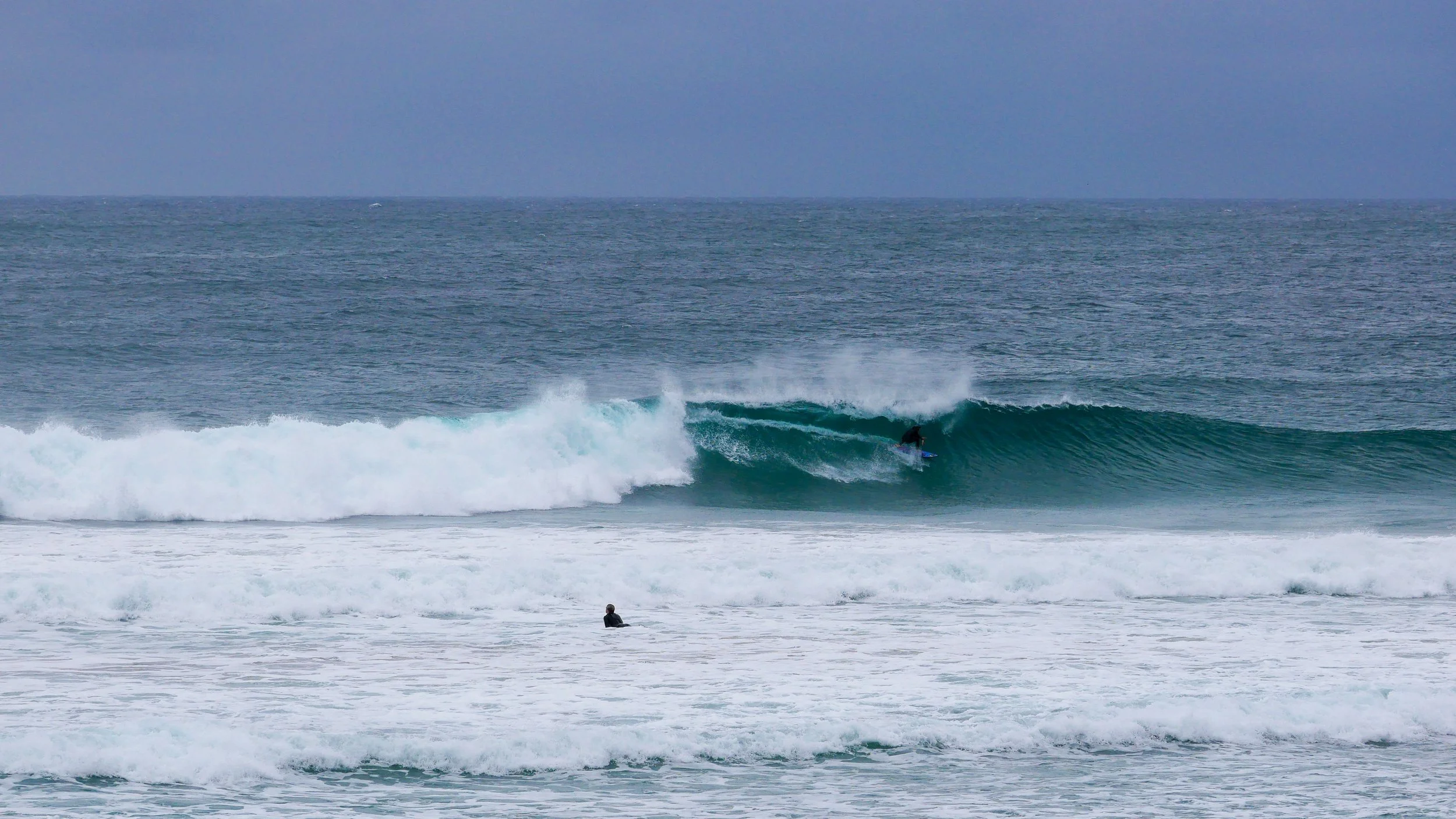 Surfer riding a wave in the ocean, another surfer watching nearby.