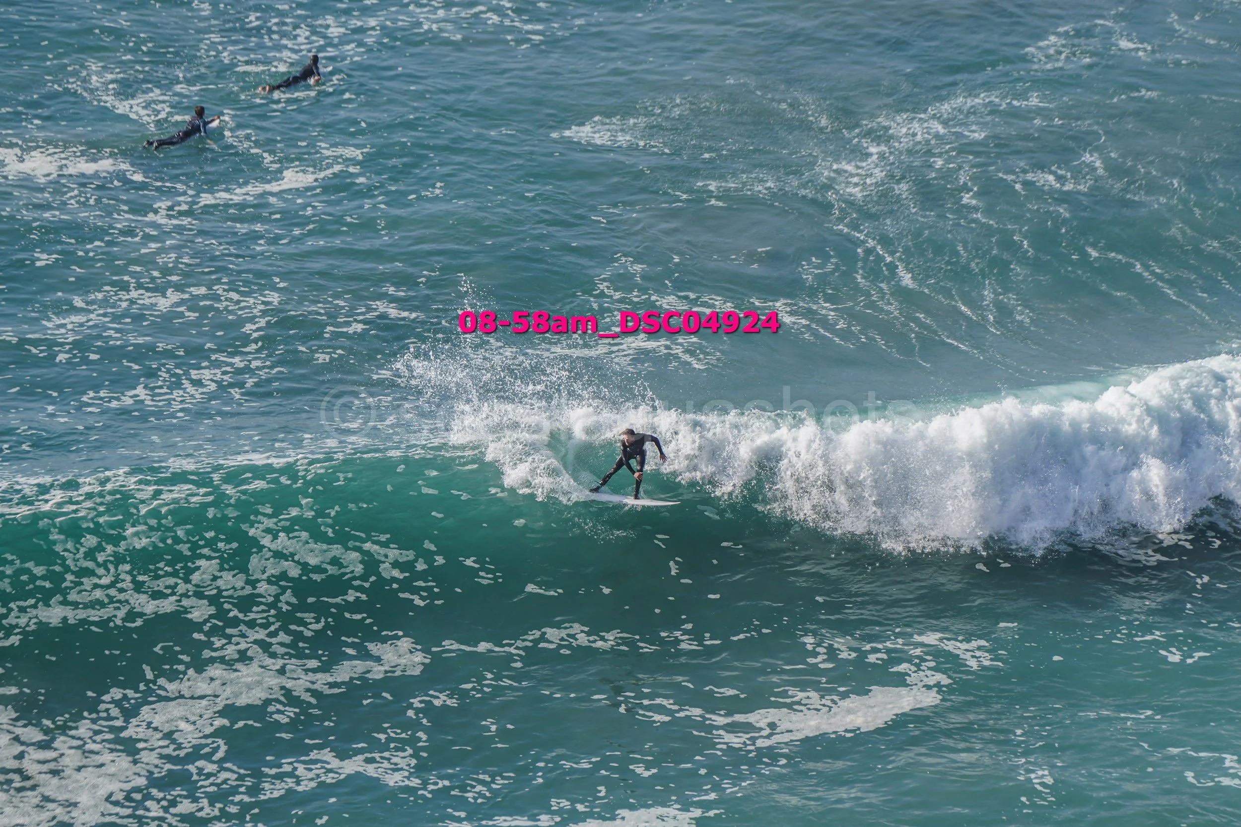 A person surfing on a wave in the ocean with two other surfers in the background.