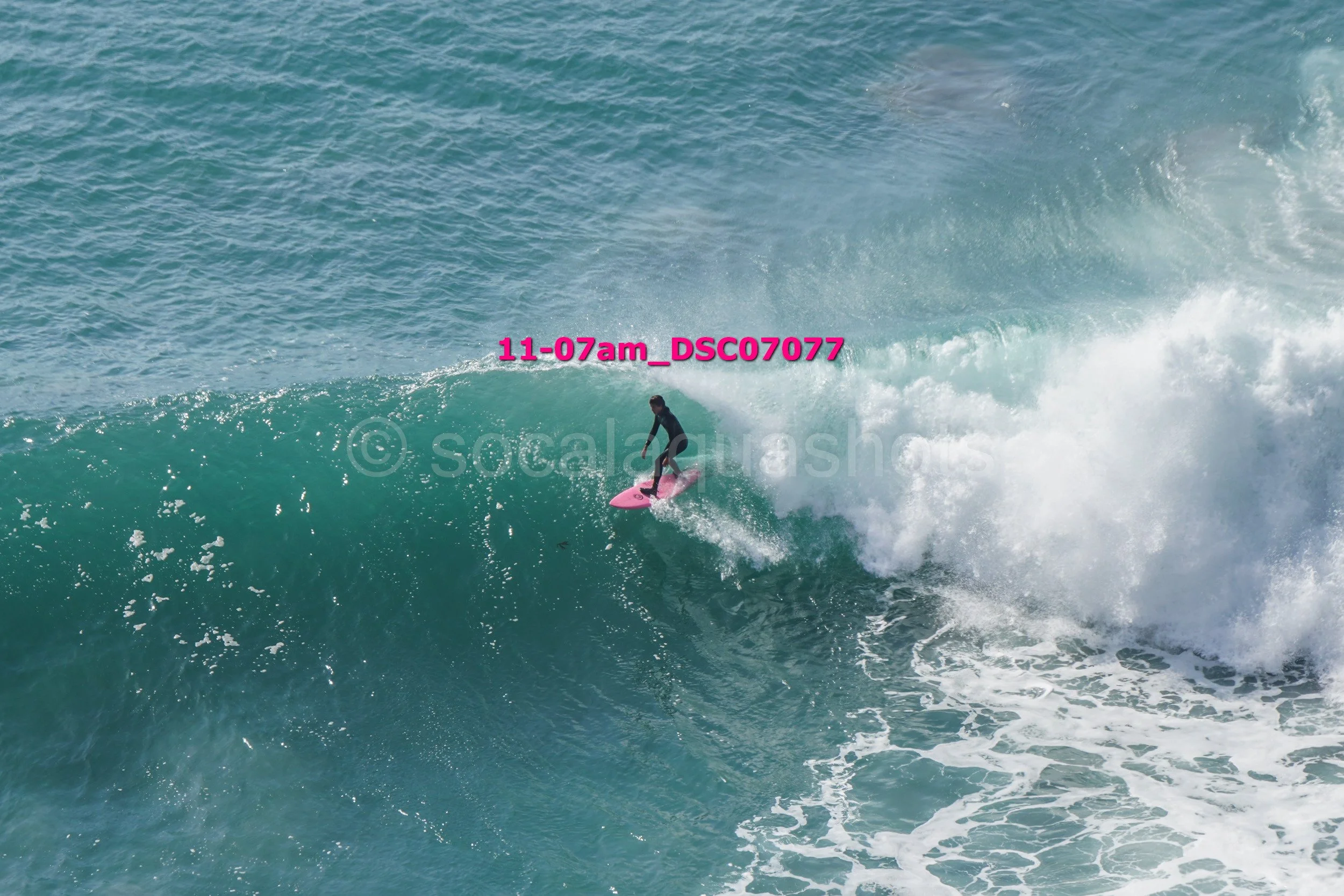 Surfer riding a wave on a pink surfboard in the ocean.
