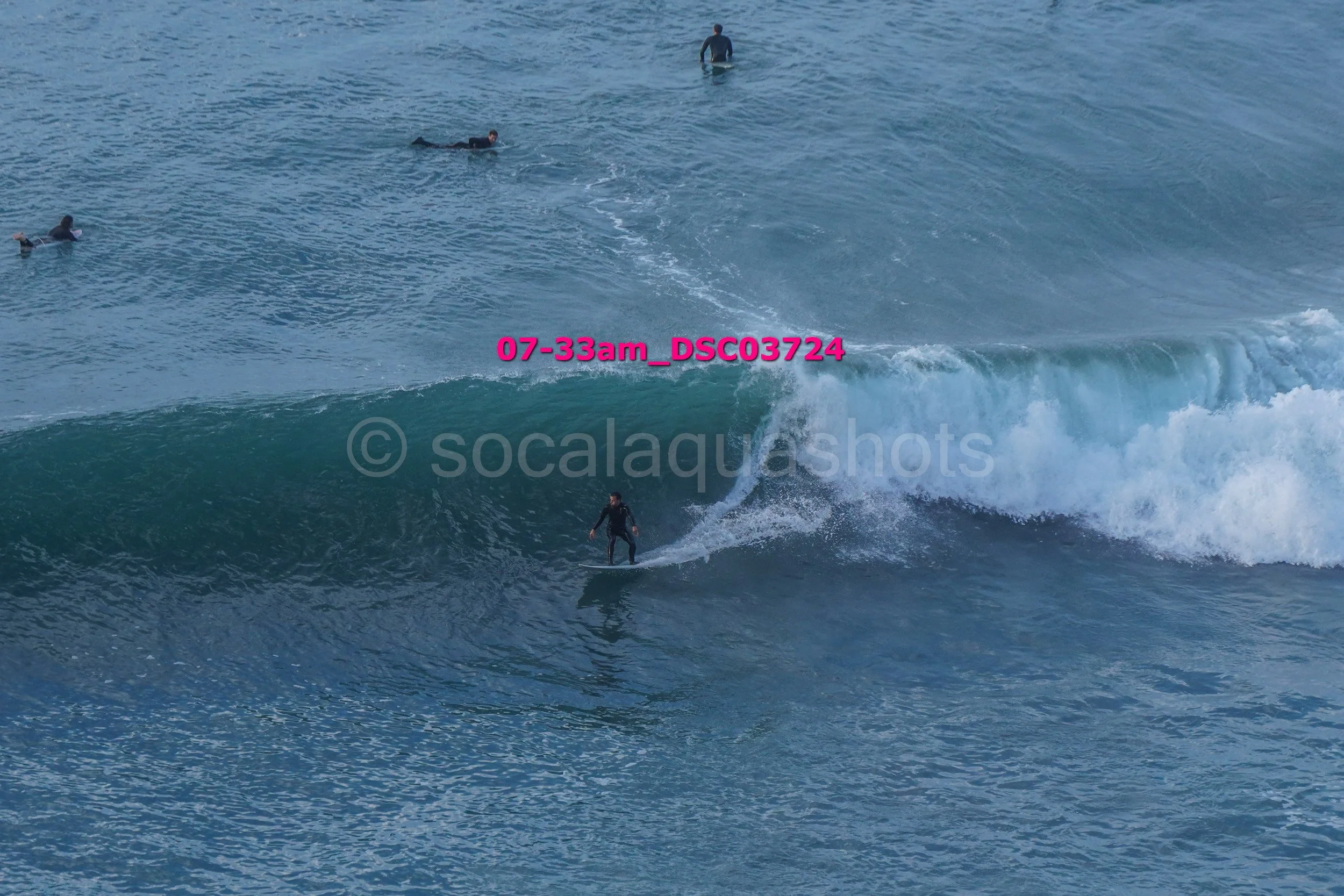 Surfer riding a wave while three other surfers are in the ocean in the background.