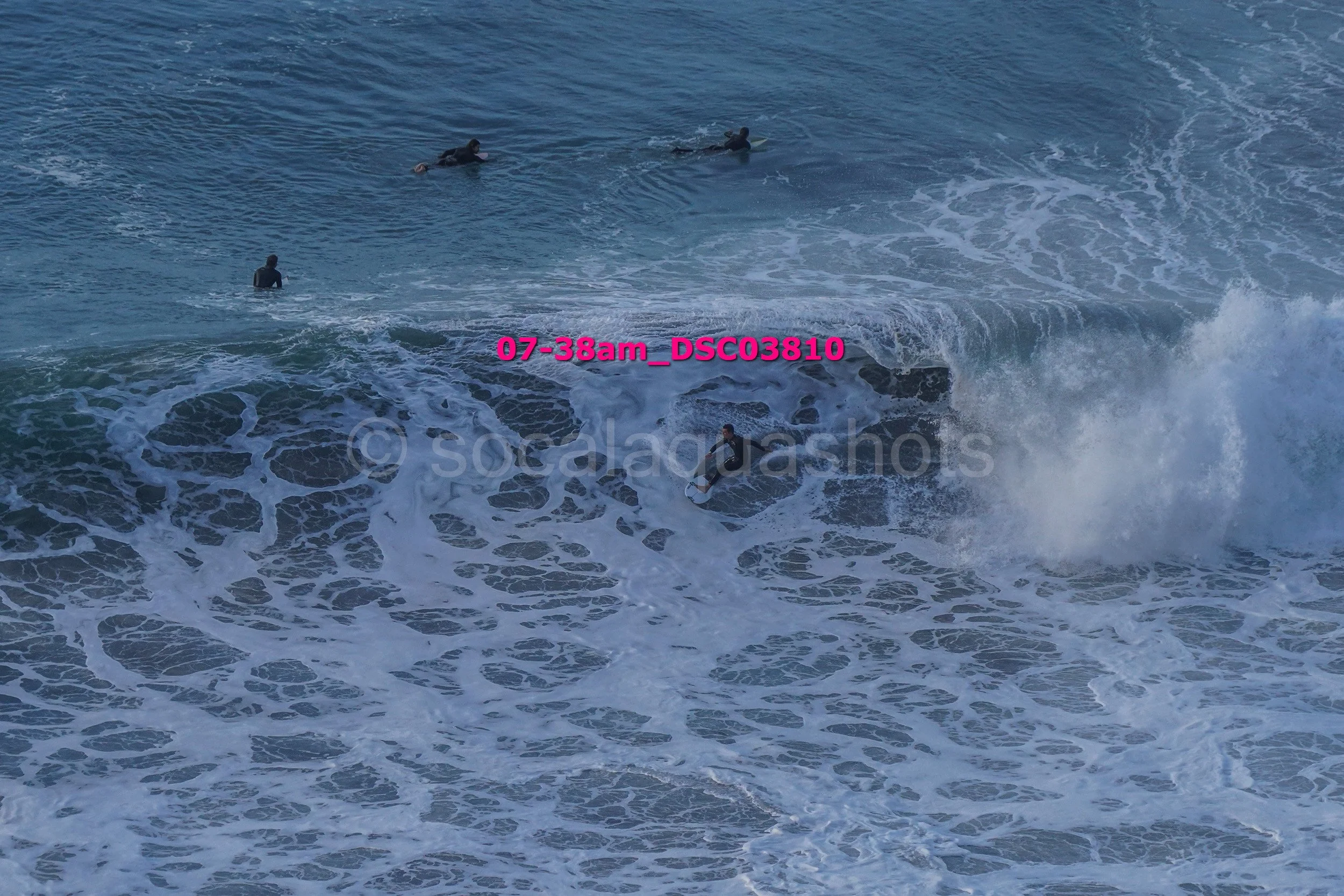 Several people surfing on ocean waves with one person standing on a surfboard and others paddling or lying on surfboards in the water.