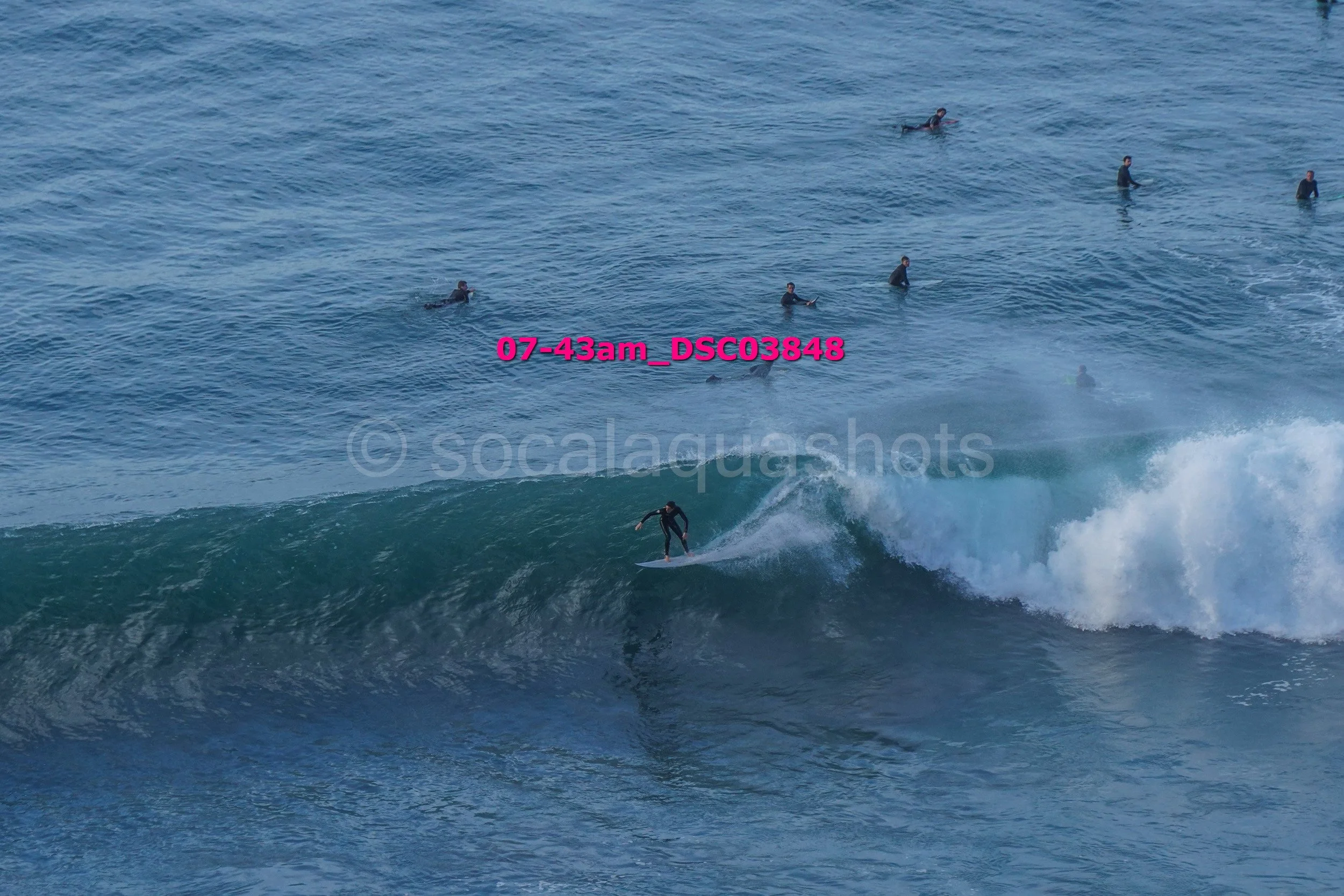 A person surfing on a wave in the ocean with several people in the water in the background.