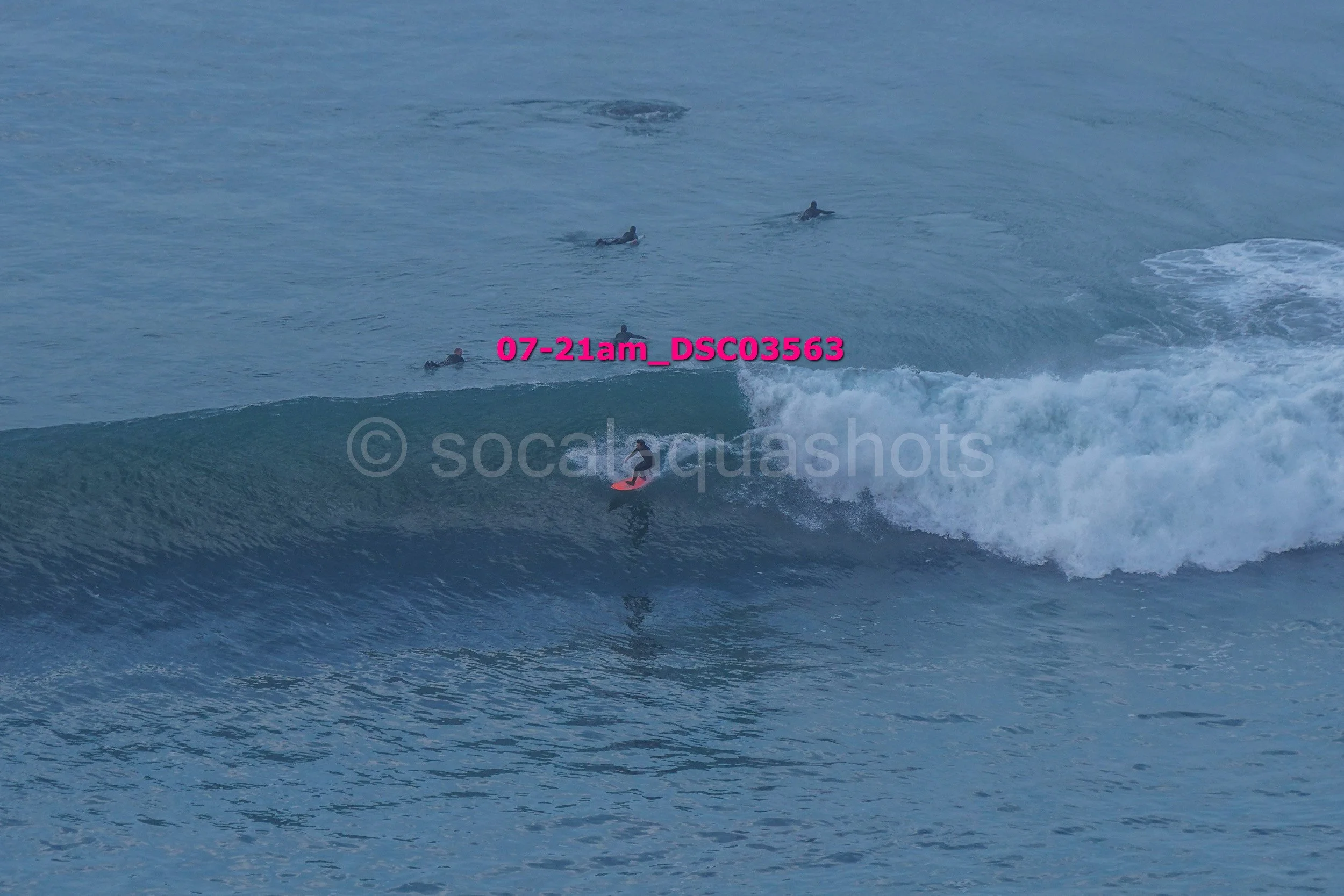 Surfer riding a wave while several surfers wait in the water nearby in the ocean.