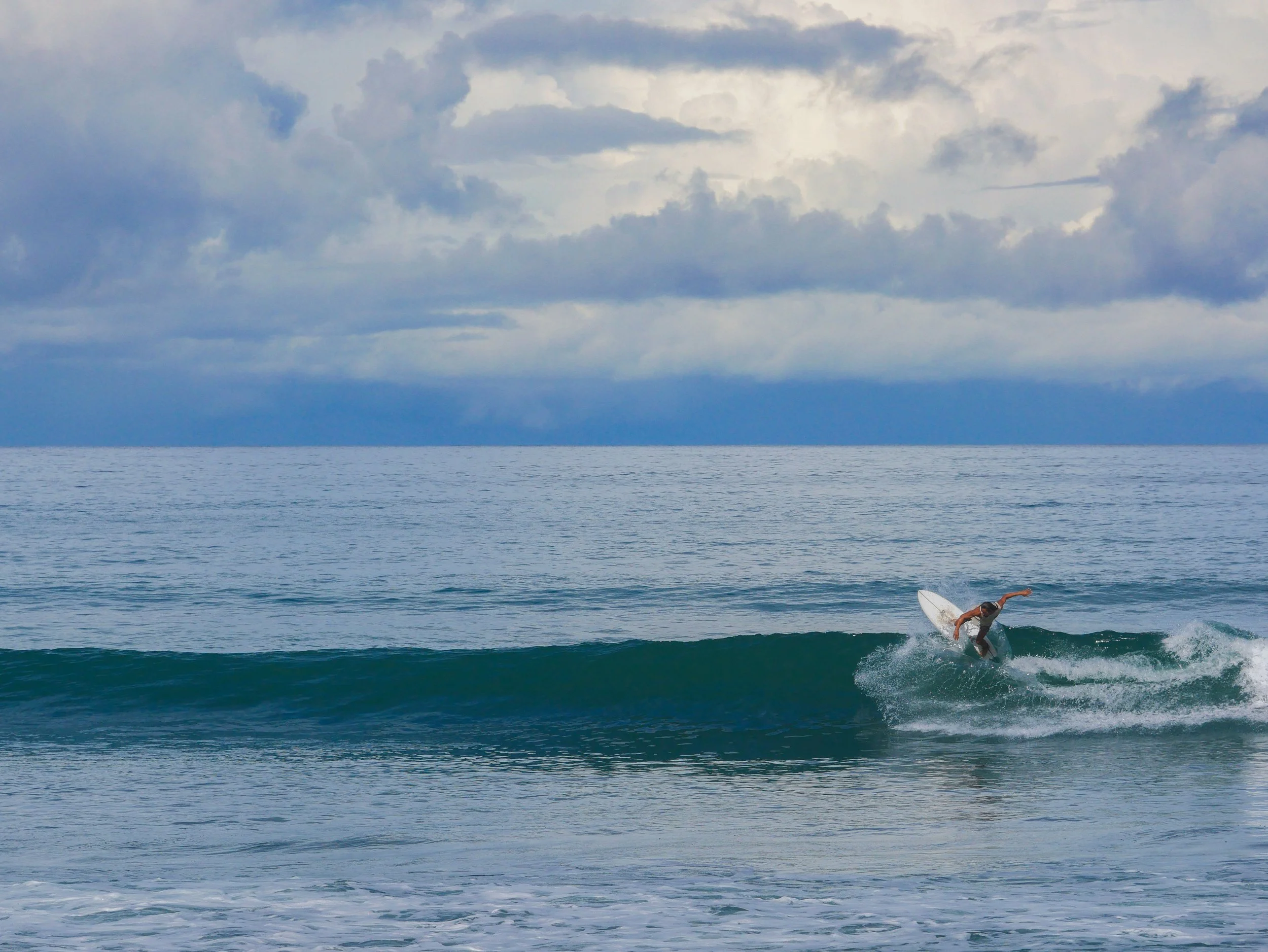 Surfer riding a wave in the ocean with cloudy skies