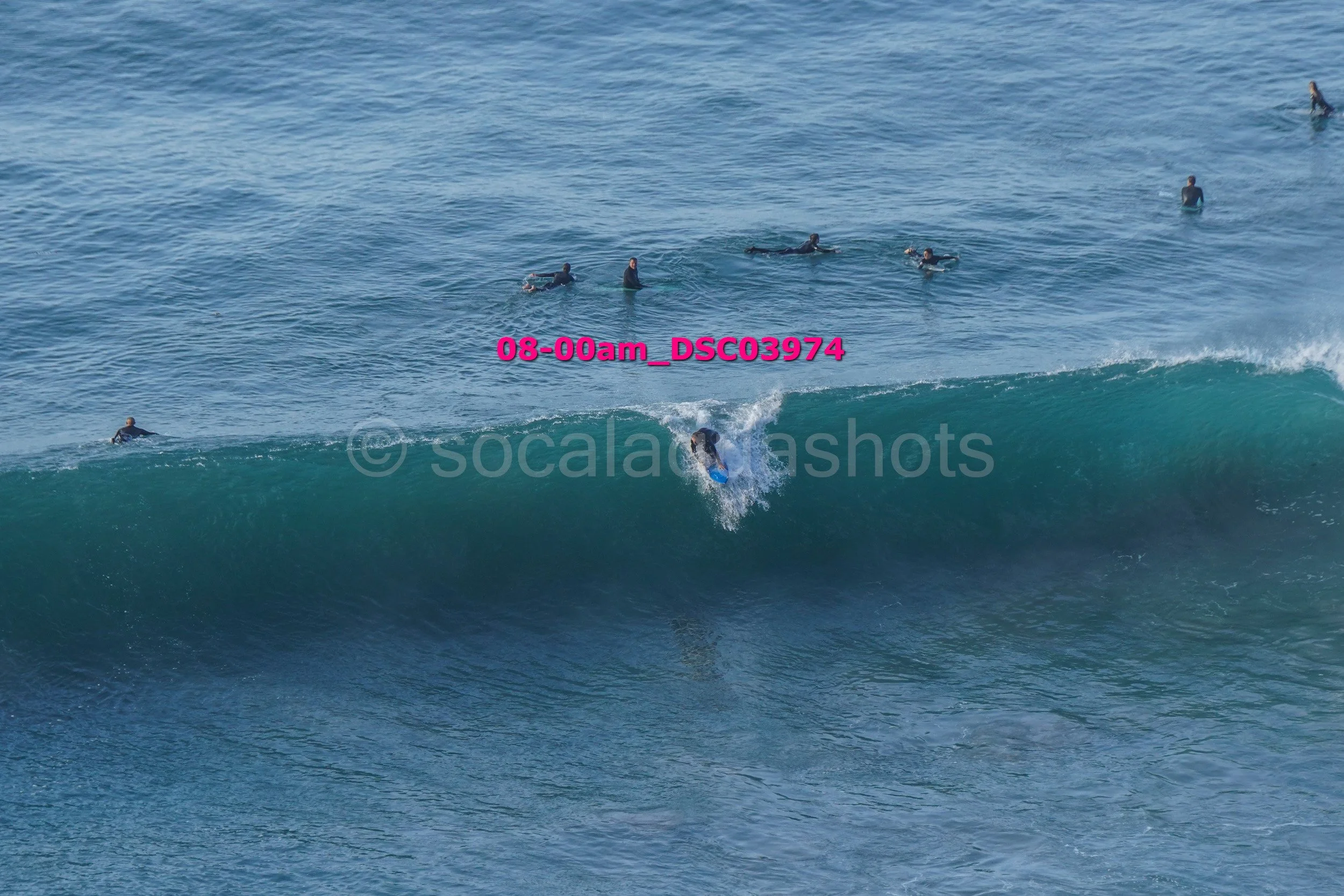 Surfer riding a wave with several people in the water watching in the background.