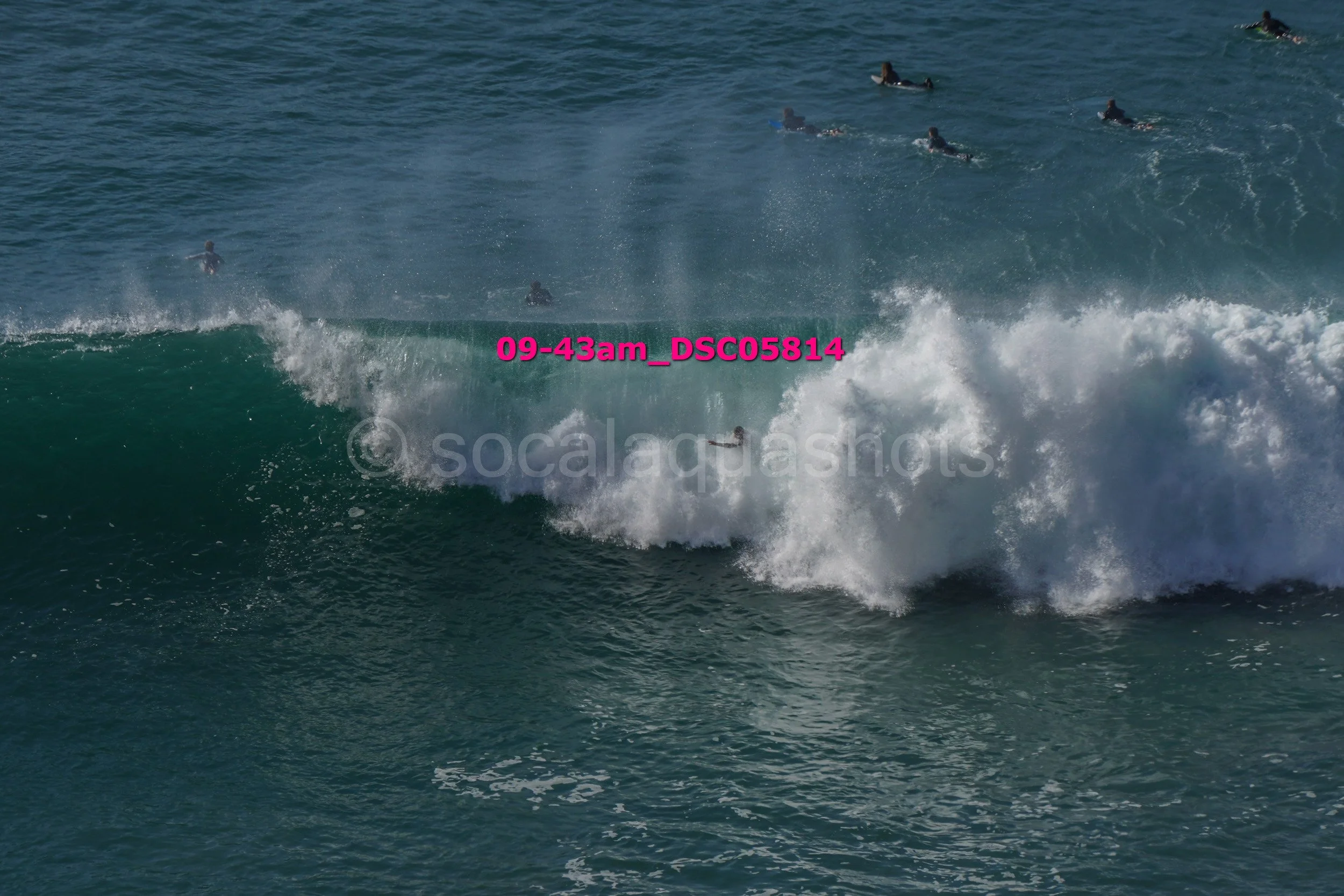 Surfer riding a wave with several people in the water in the background.