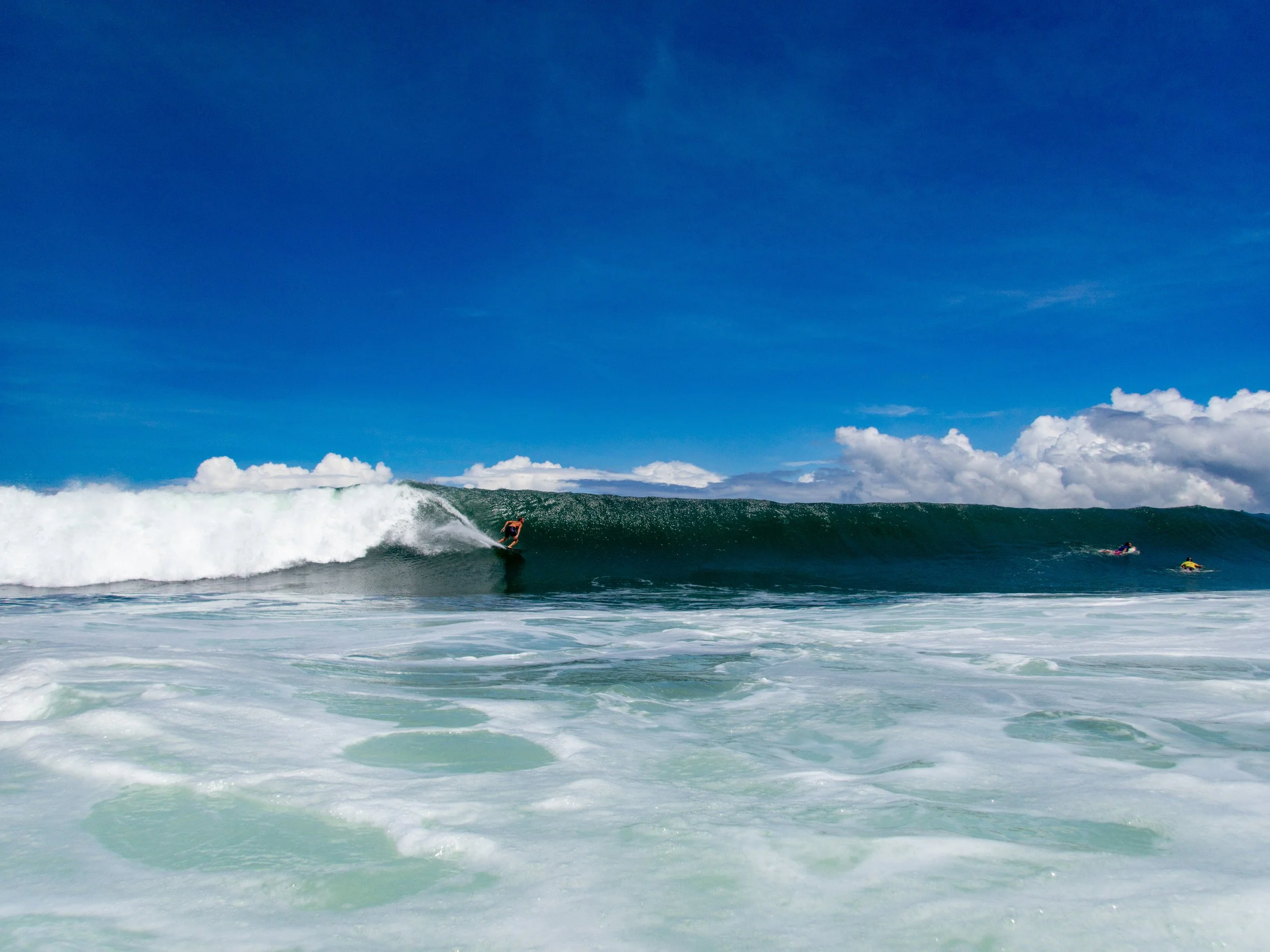 Surfer riding a large ocean wave with blue sky and clouds
