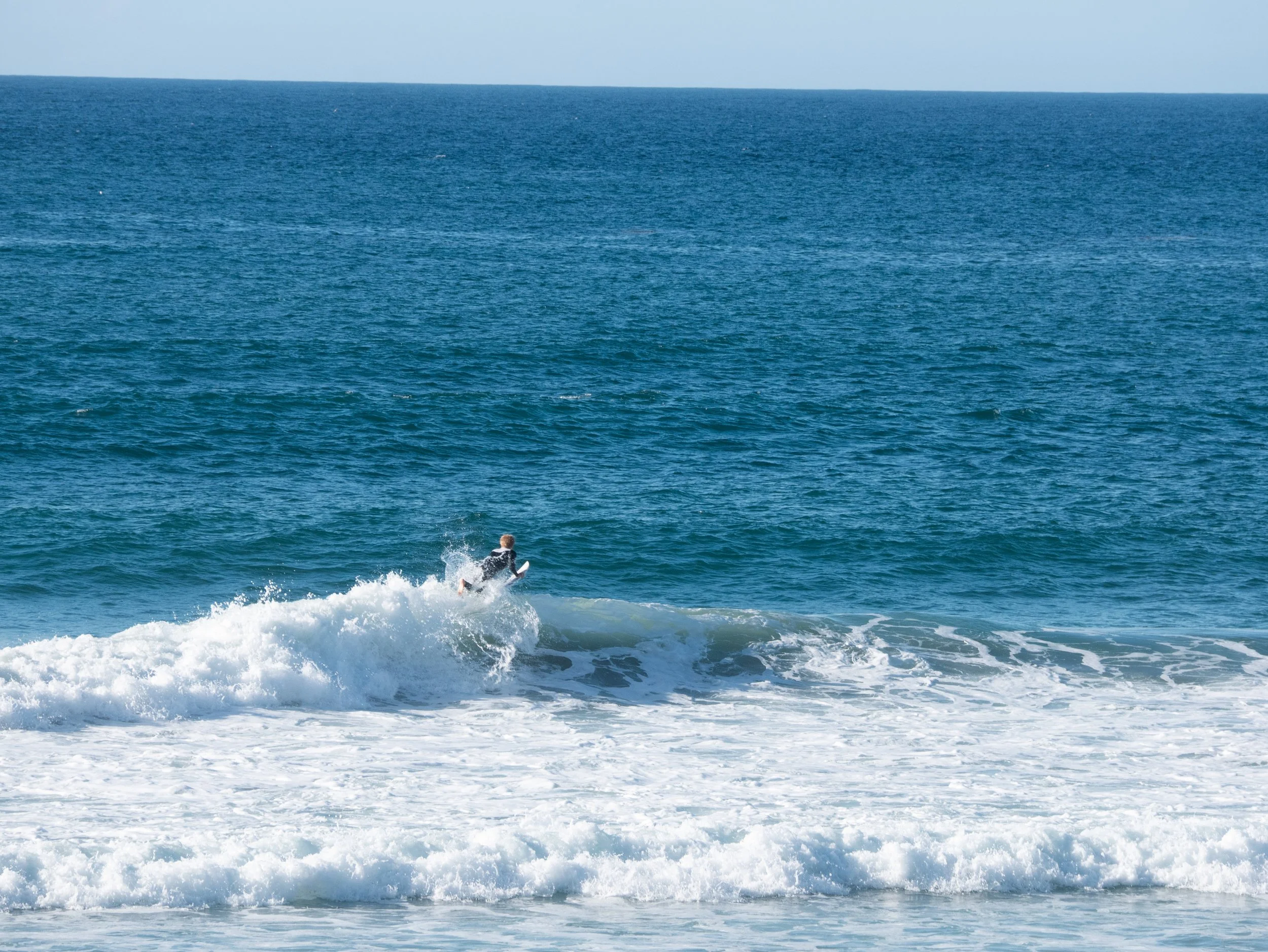 Person surfing on a wave in the ocean on a clear day.
