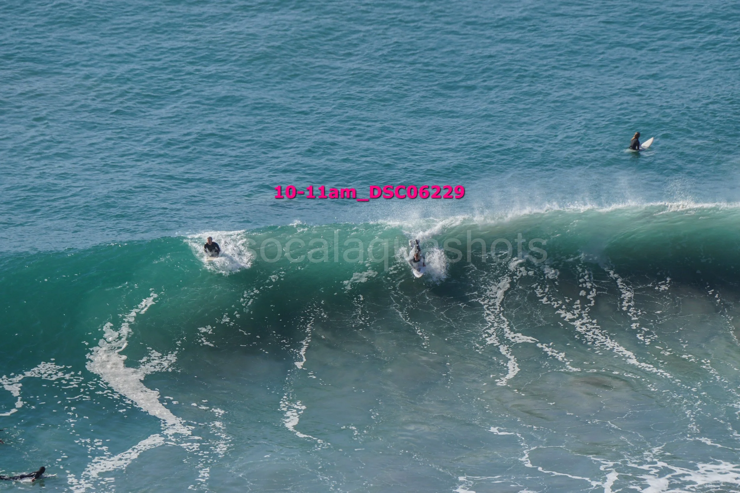 Surfers riding a large wave near the shore with one surfer in the water on a surfboard to the right