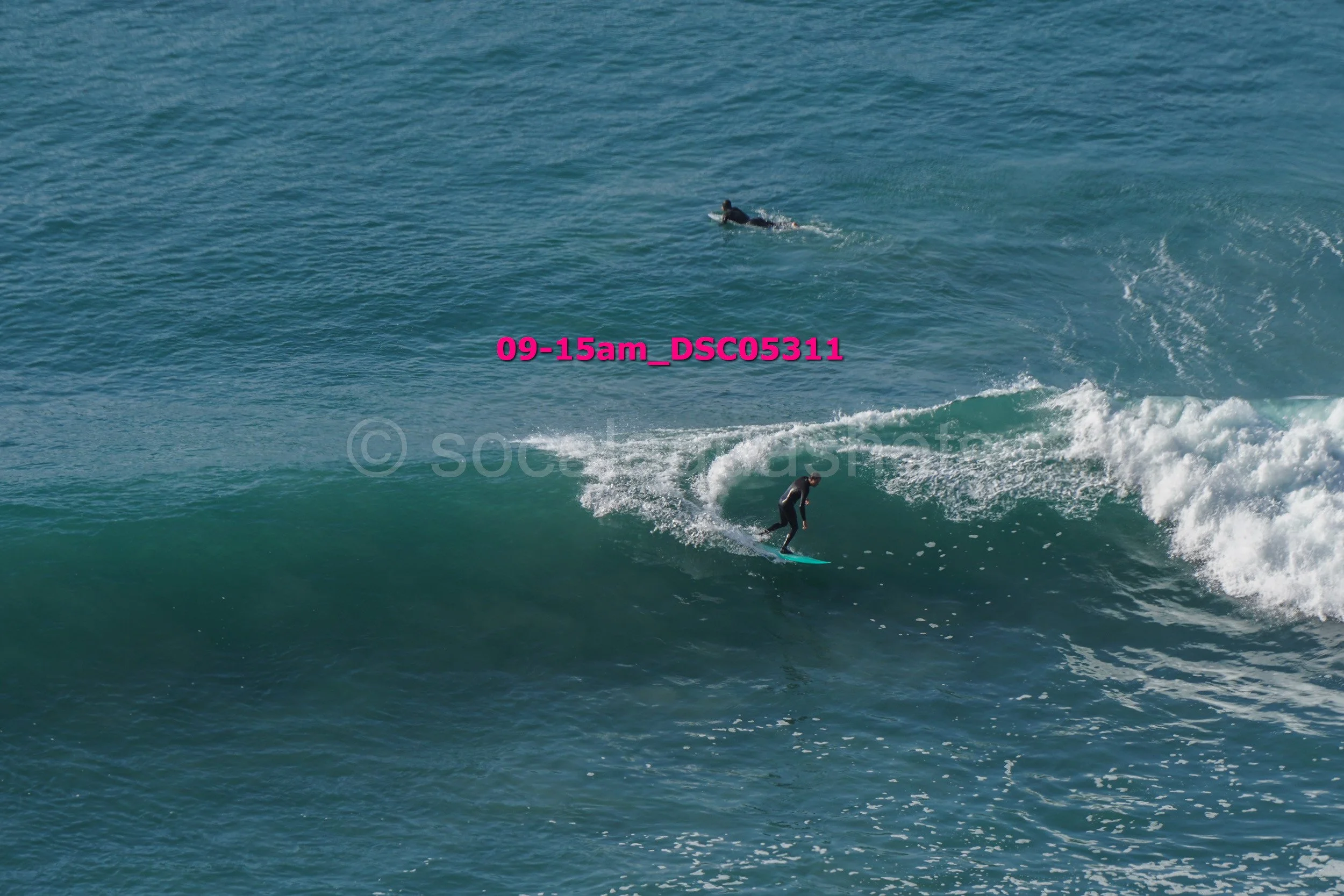 A person surfing a wave in the ocean with a swimmer in the background
