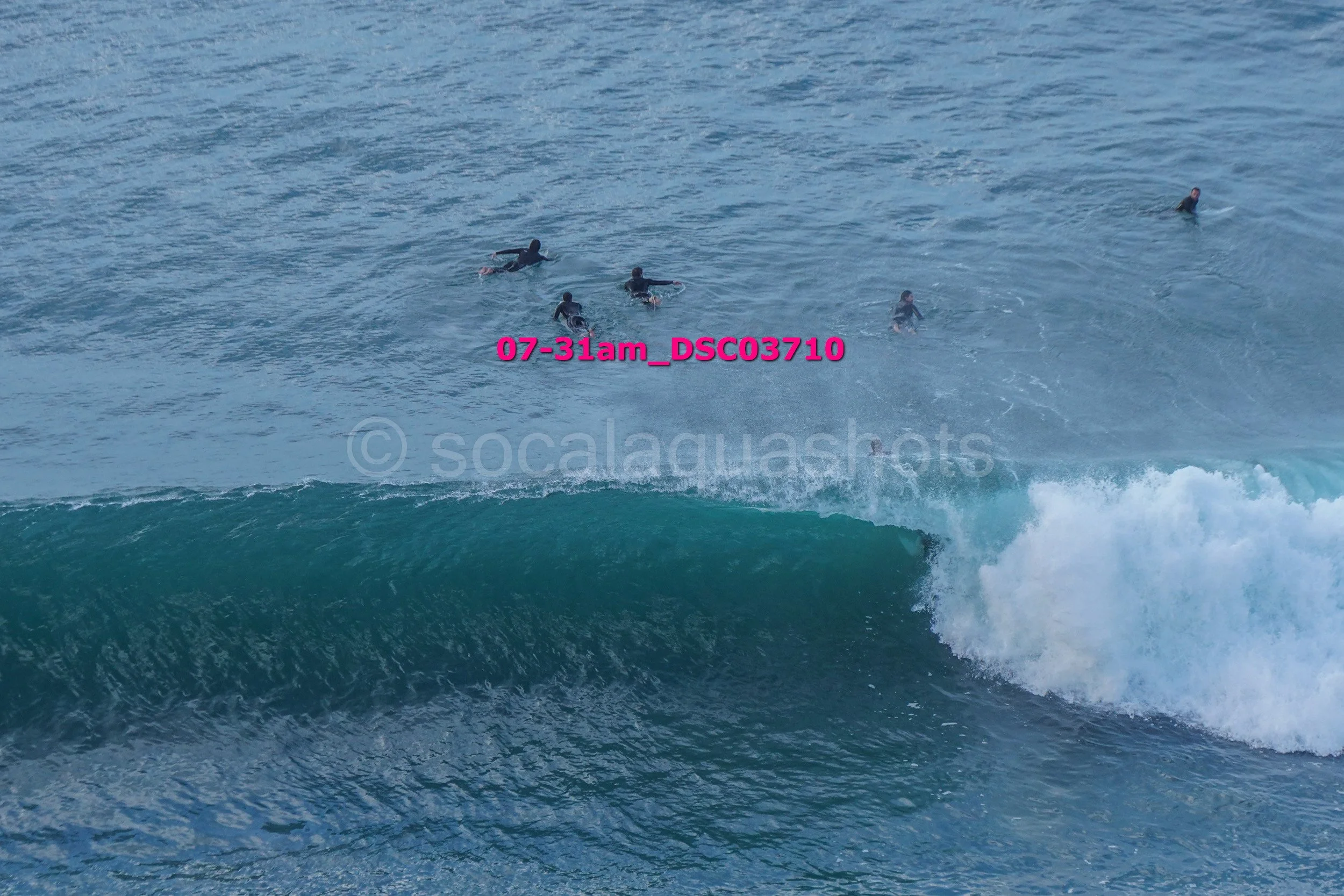 Five people swimming in the ocean near a breaking wave.