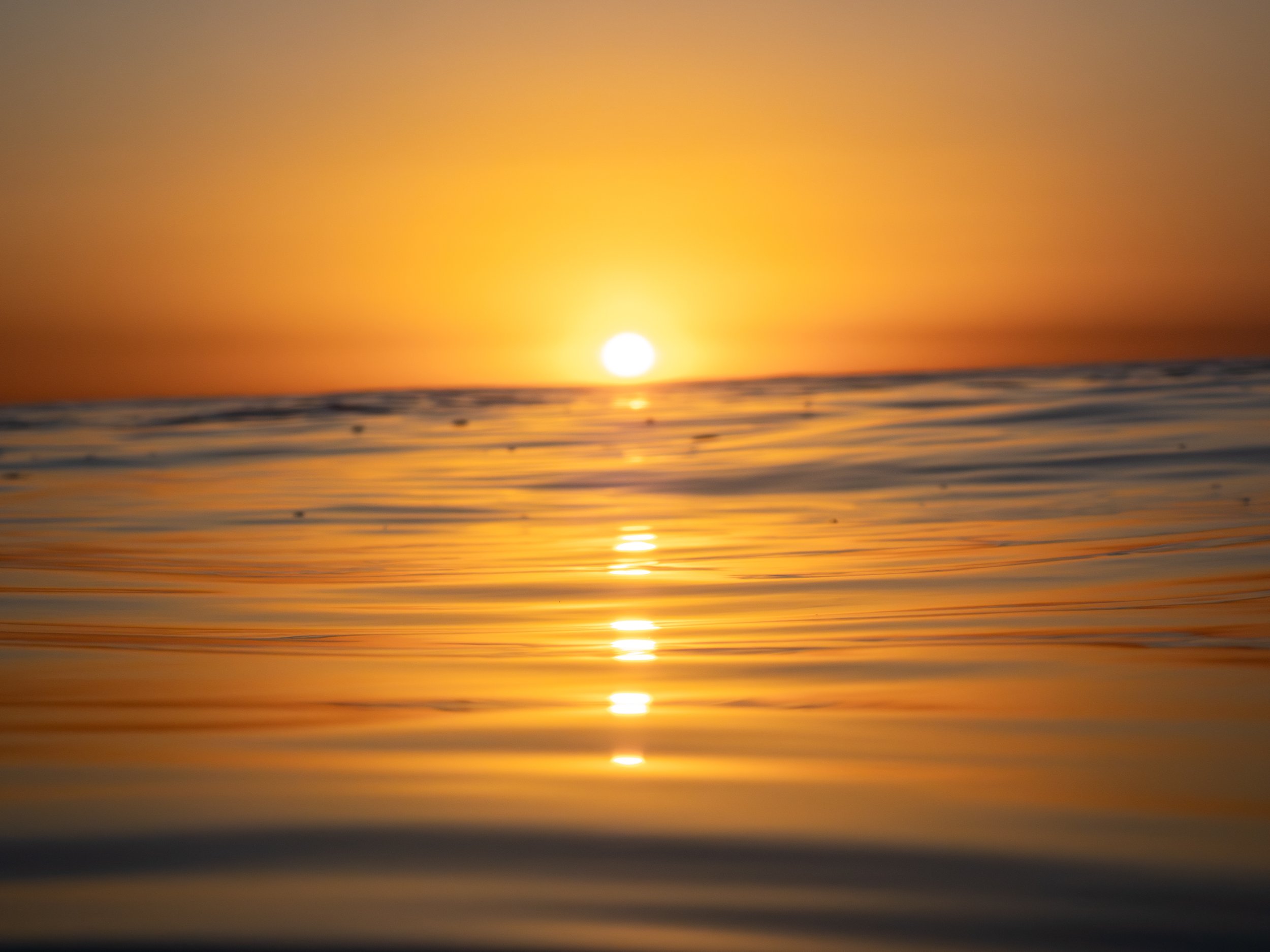 A sunset over the ocean, with the sun partially below the horizon and its reflection on the water.