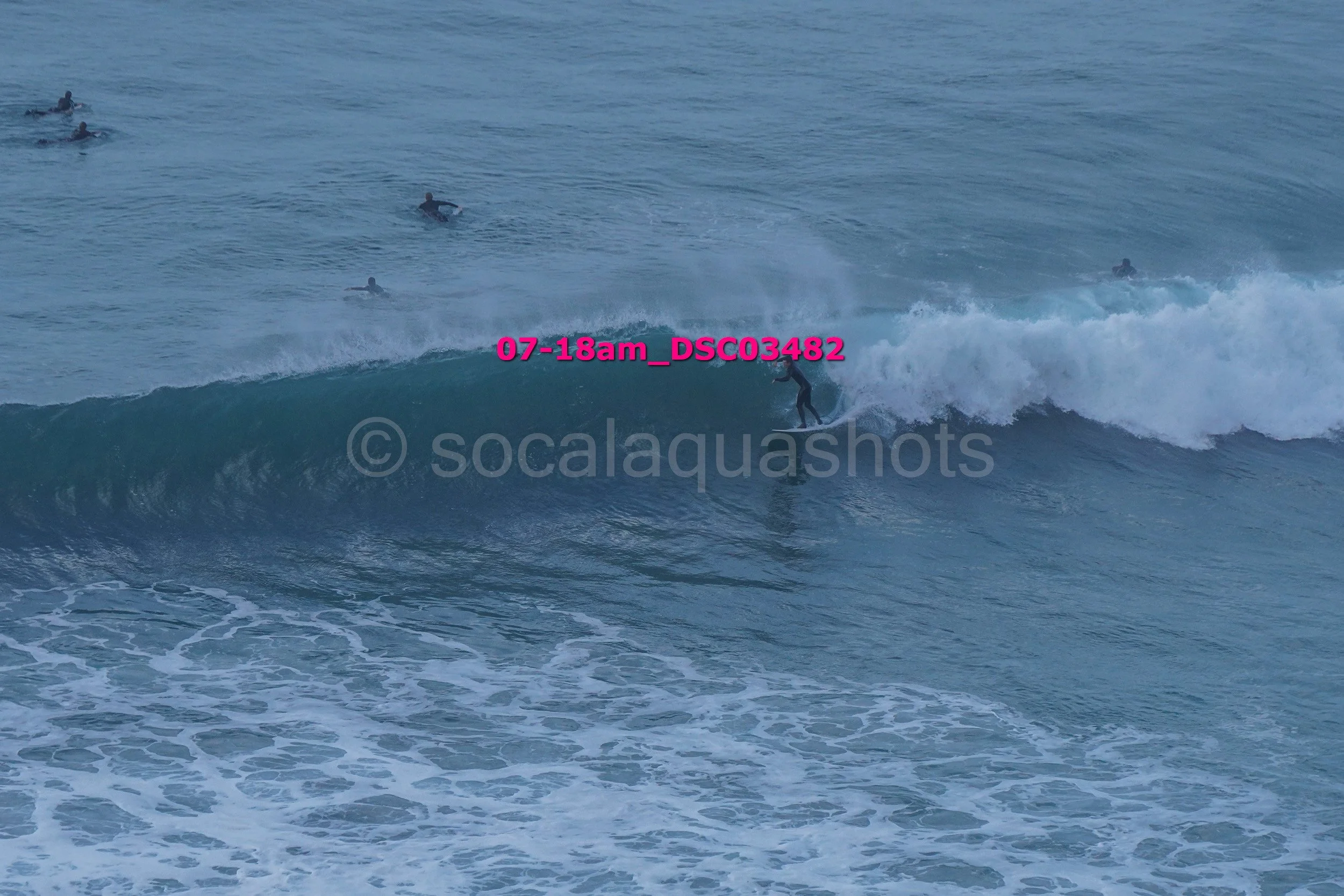 A person surfing on a wave in the ocean with several other surfers in the background.