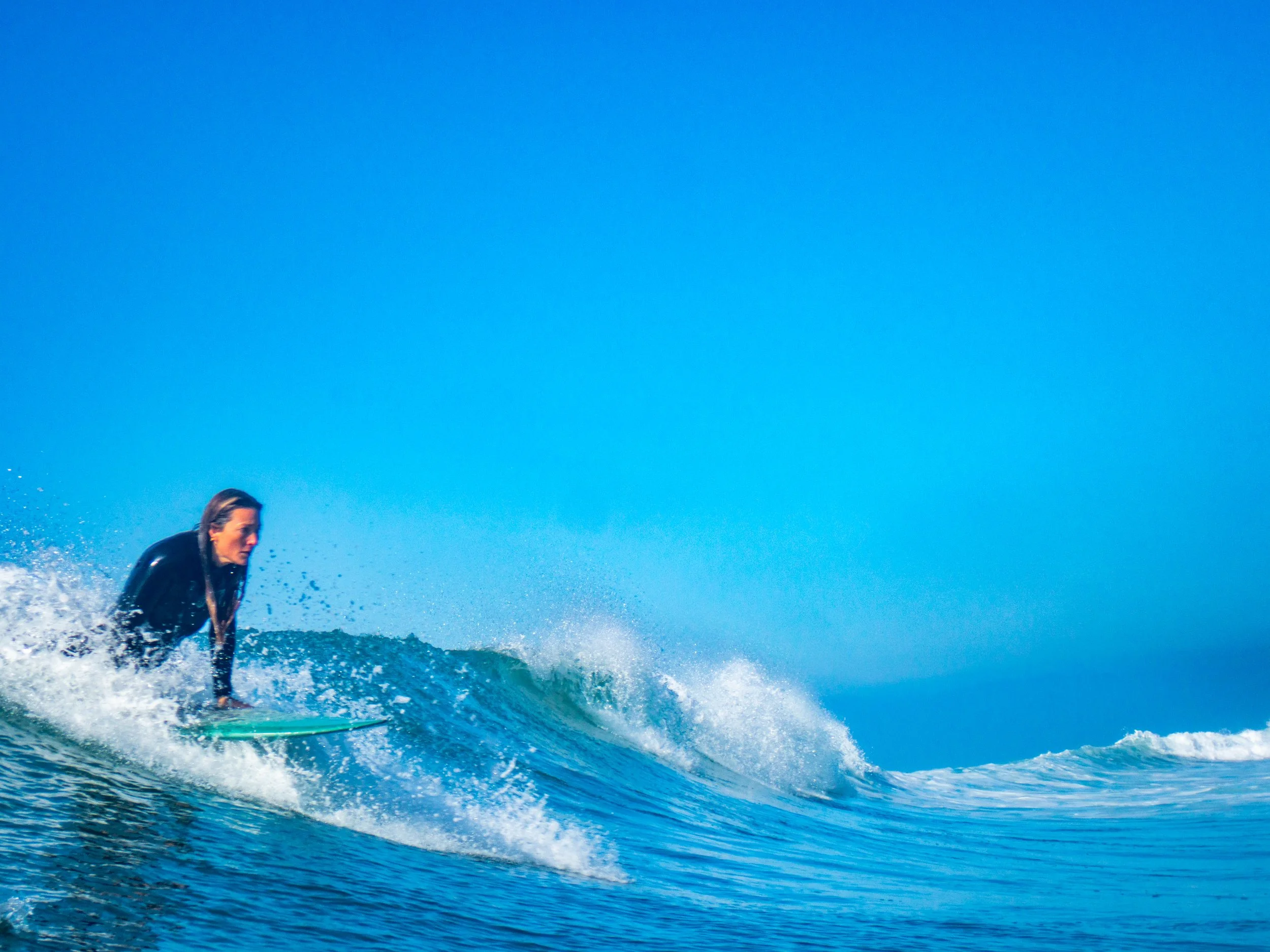 A woman surfing on a wave in the ocean on a clear sunny day.