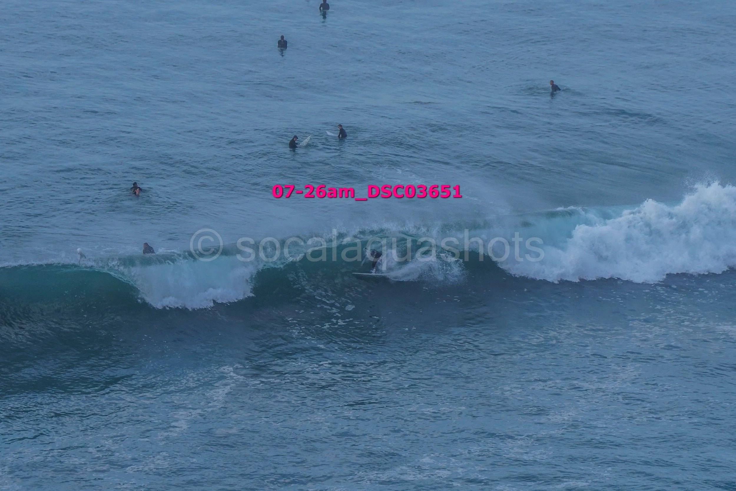 Surfer riding a wave in the ocean with multiple surfers in the water in the background.