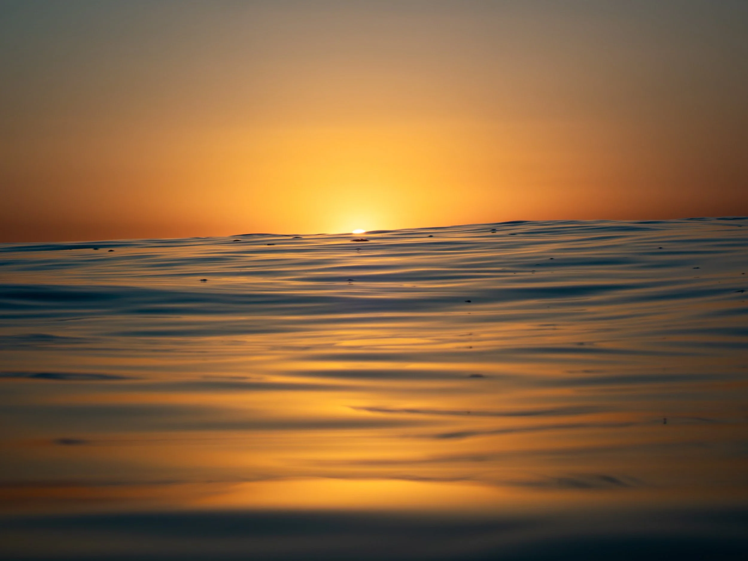 A sunset over calm ocean water with gentle ripples, displaying warm orange and yellow hues.