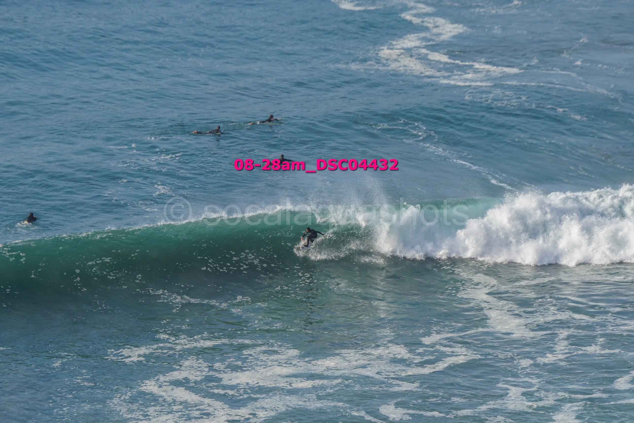 A person surfing on a wave in the ocean with several other surfers in the water nearby.