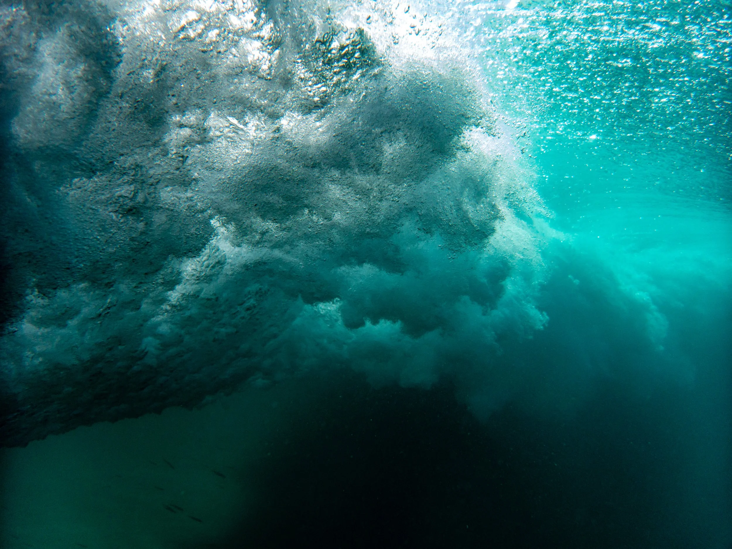 Underwater view of a large wave breaking and bubbles forming beneath the surface.