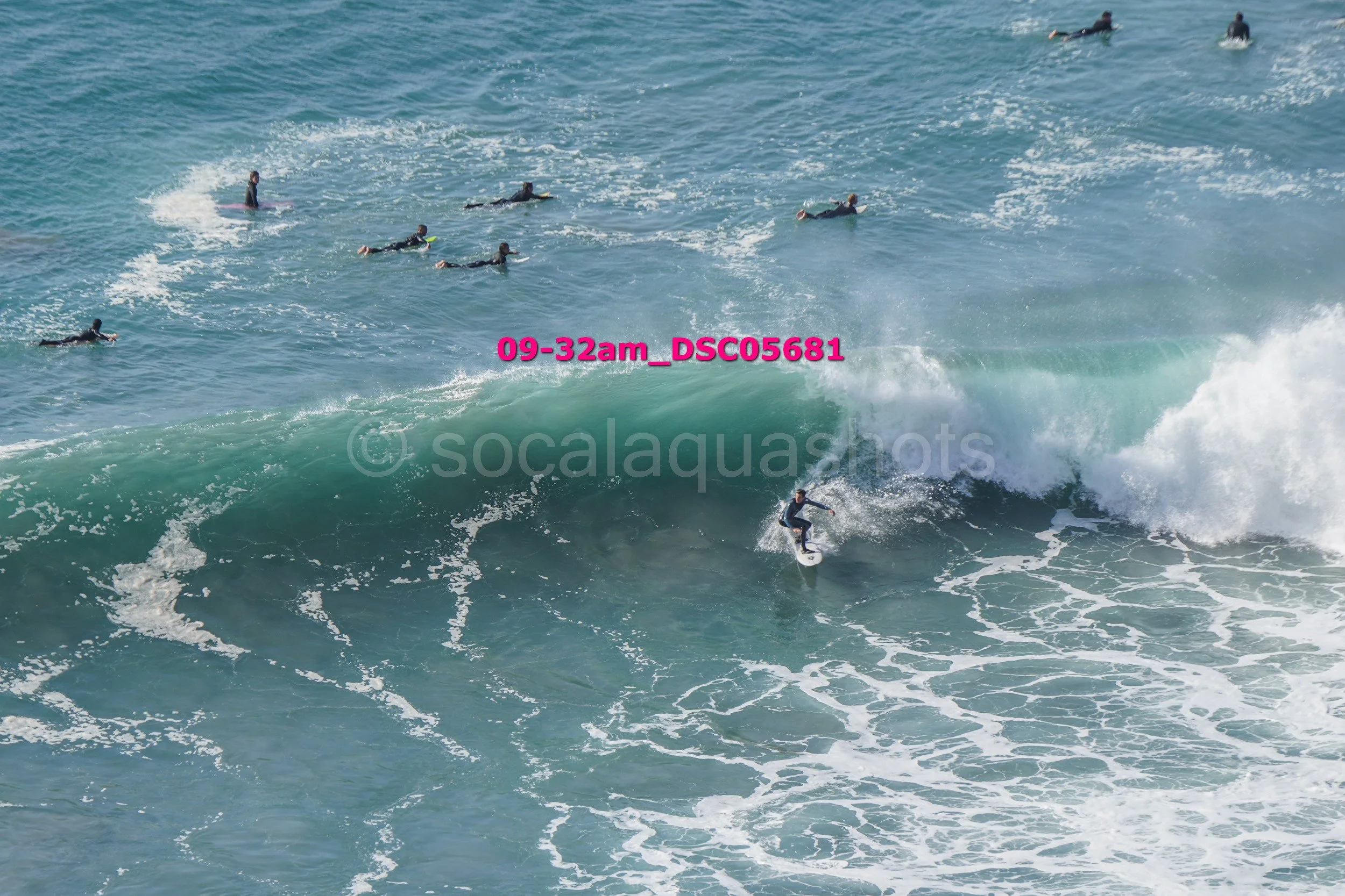 A surfer riding a wave with multiple surfers swimming in the ocean nearby.
