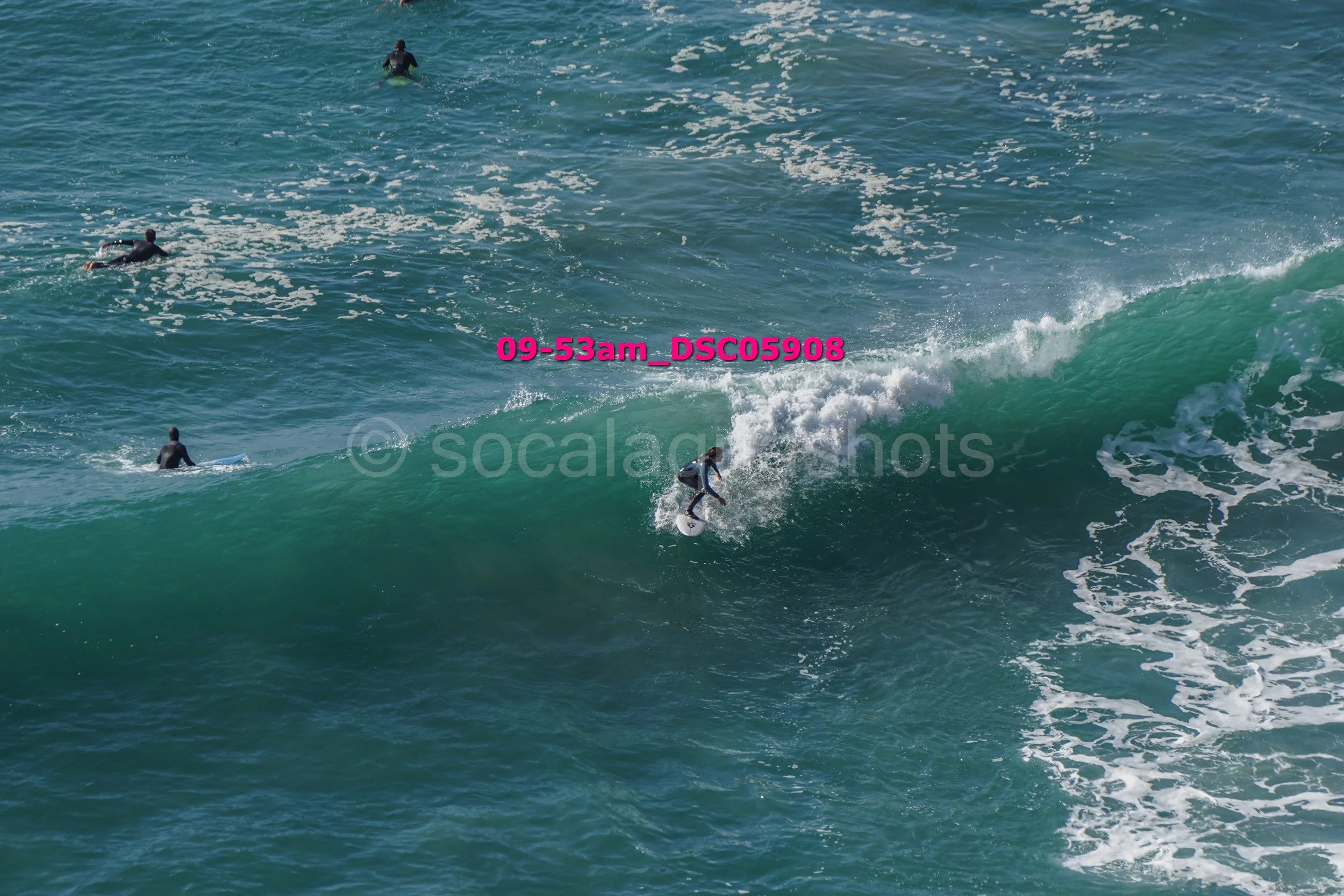 Surfer riding a large wave with three other surfers in the water nearby.