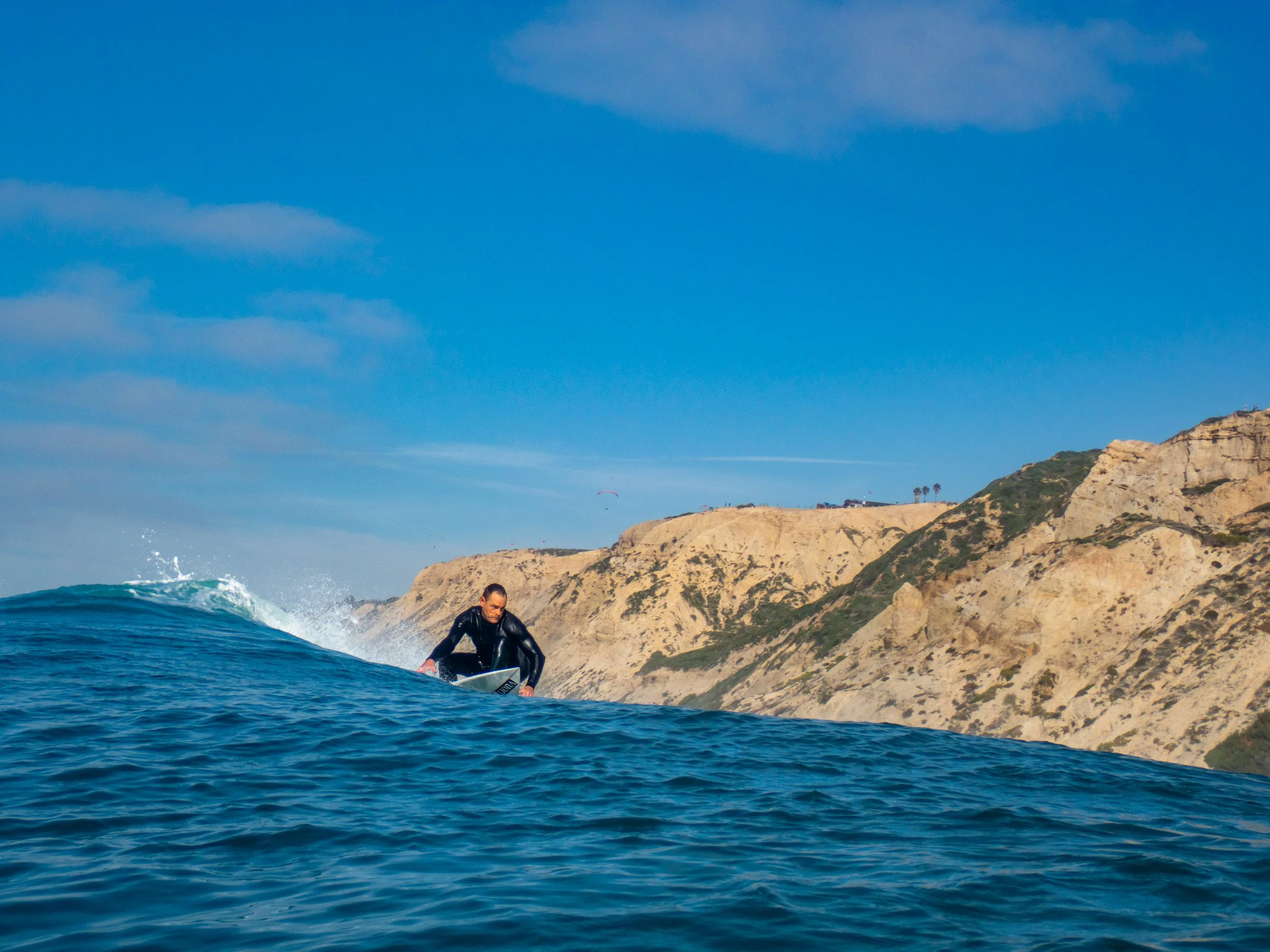 A man surfing in the ocean with cliffs in the background on a clear day.