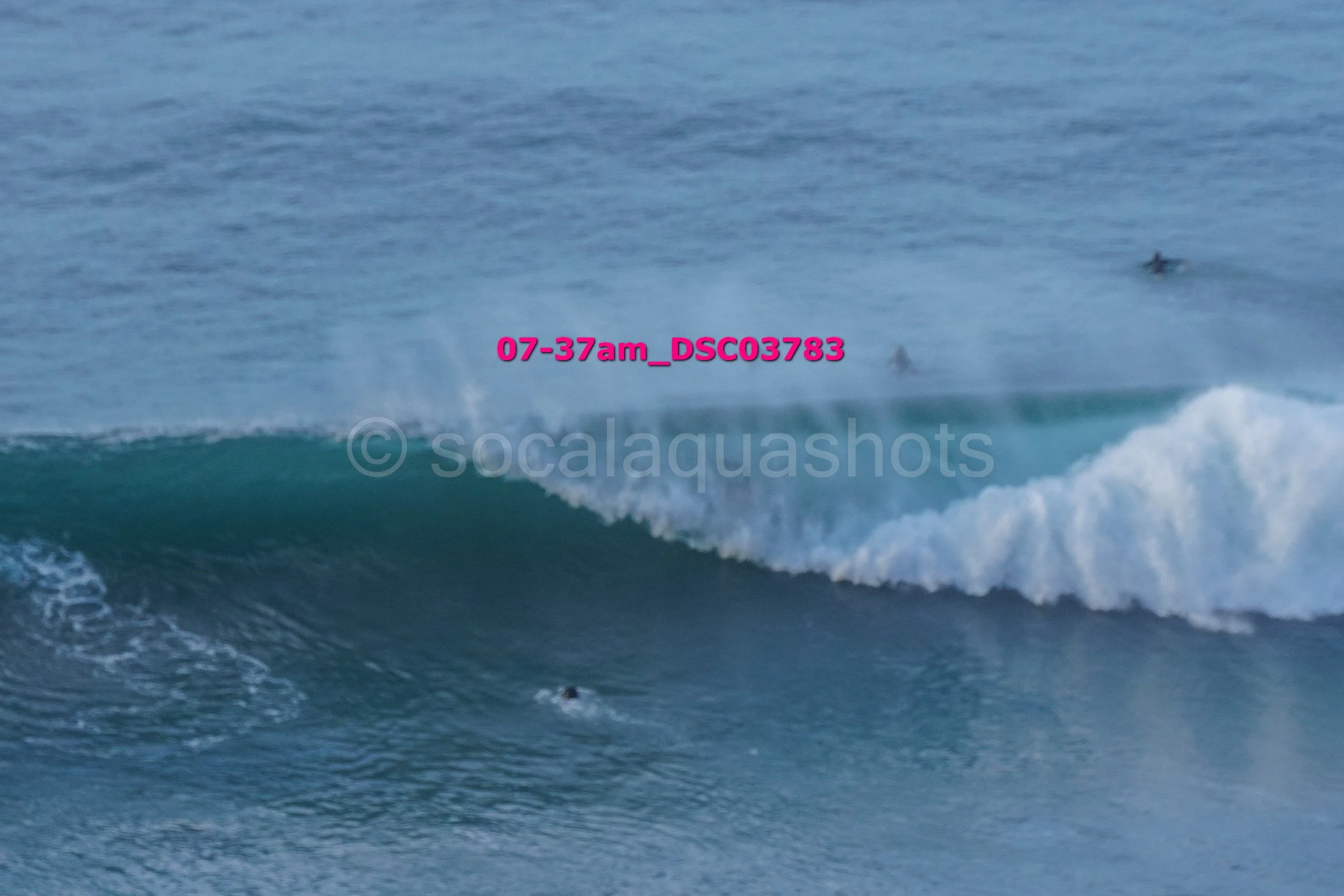 Ocean waves with surfers in the distance, approaching the shoreline.