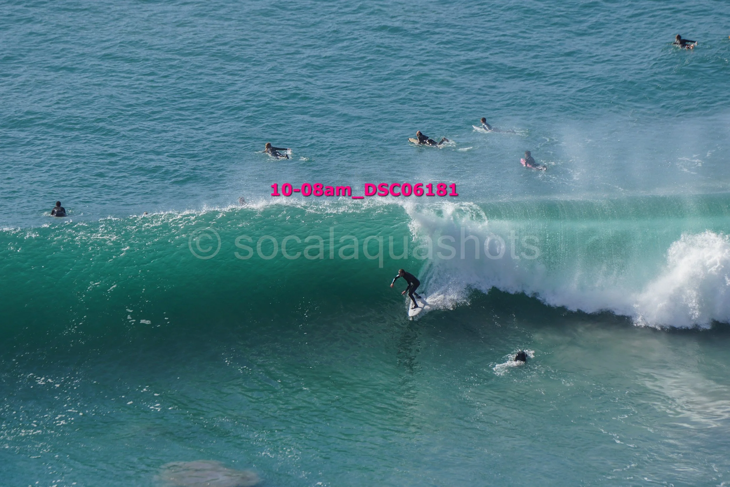 Surfer riding a wave with multiple people in the water in the background.