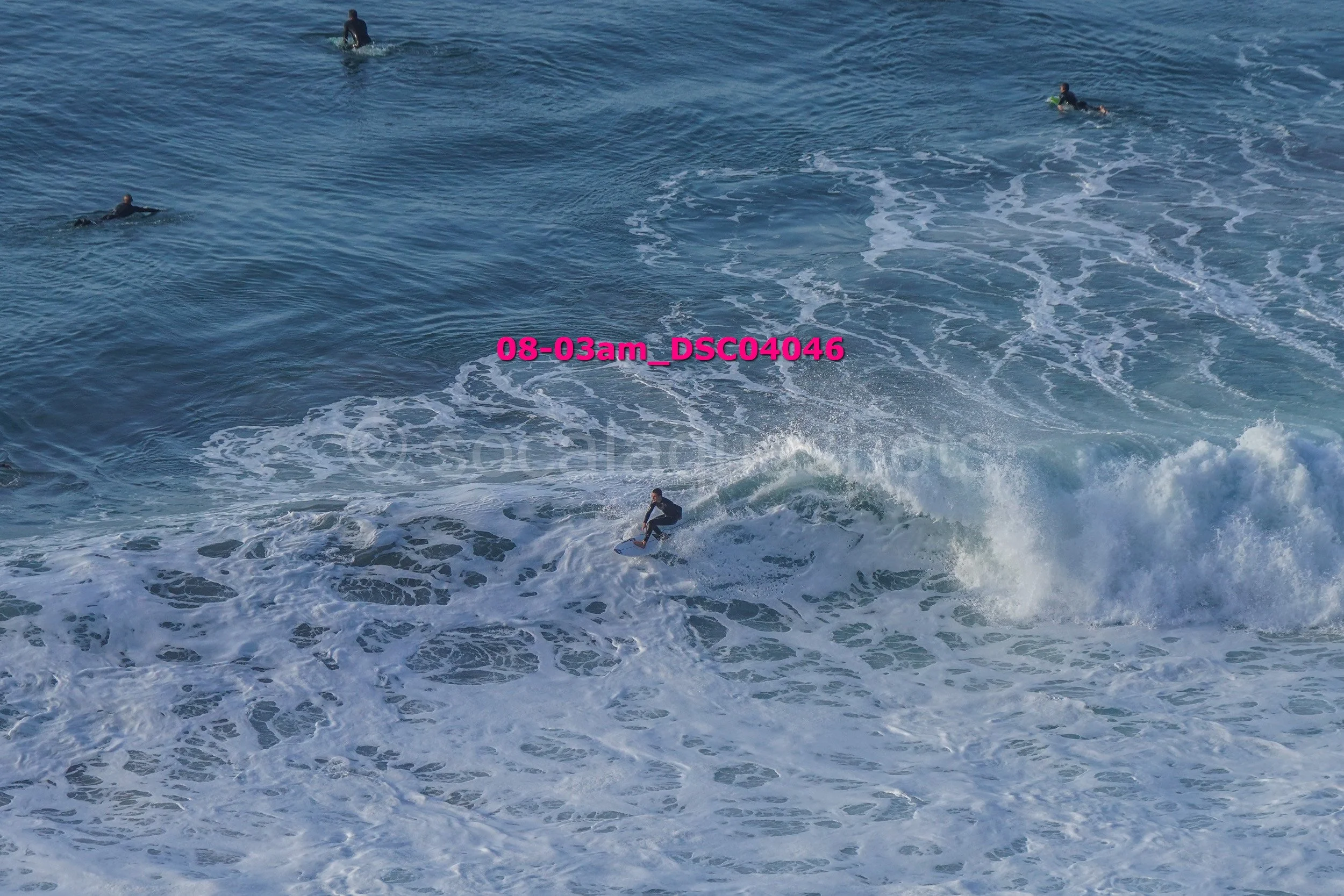 Surfer riding a wave in the ocean with other people swimming nearby.
