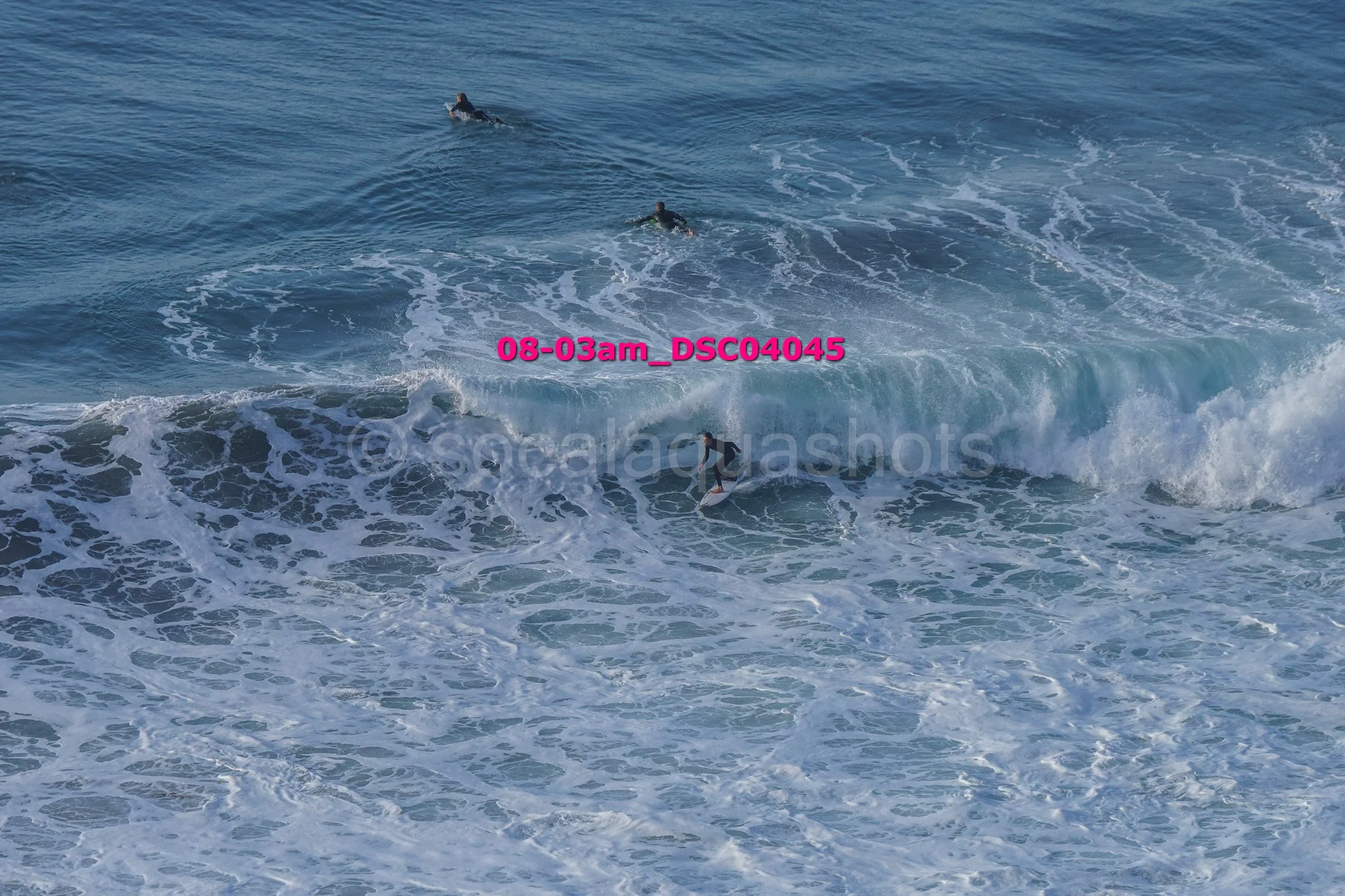 Multiple surfers riding ocean waves, some on surfboards, in the sea with foam and water spray.