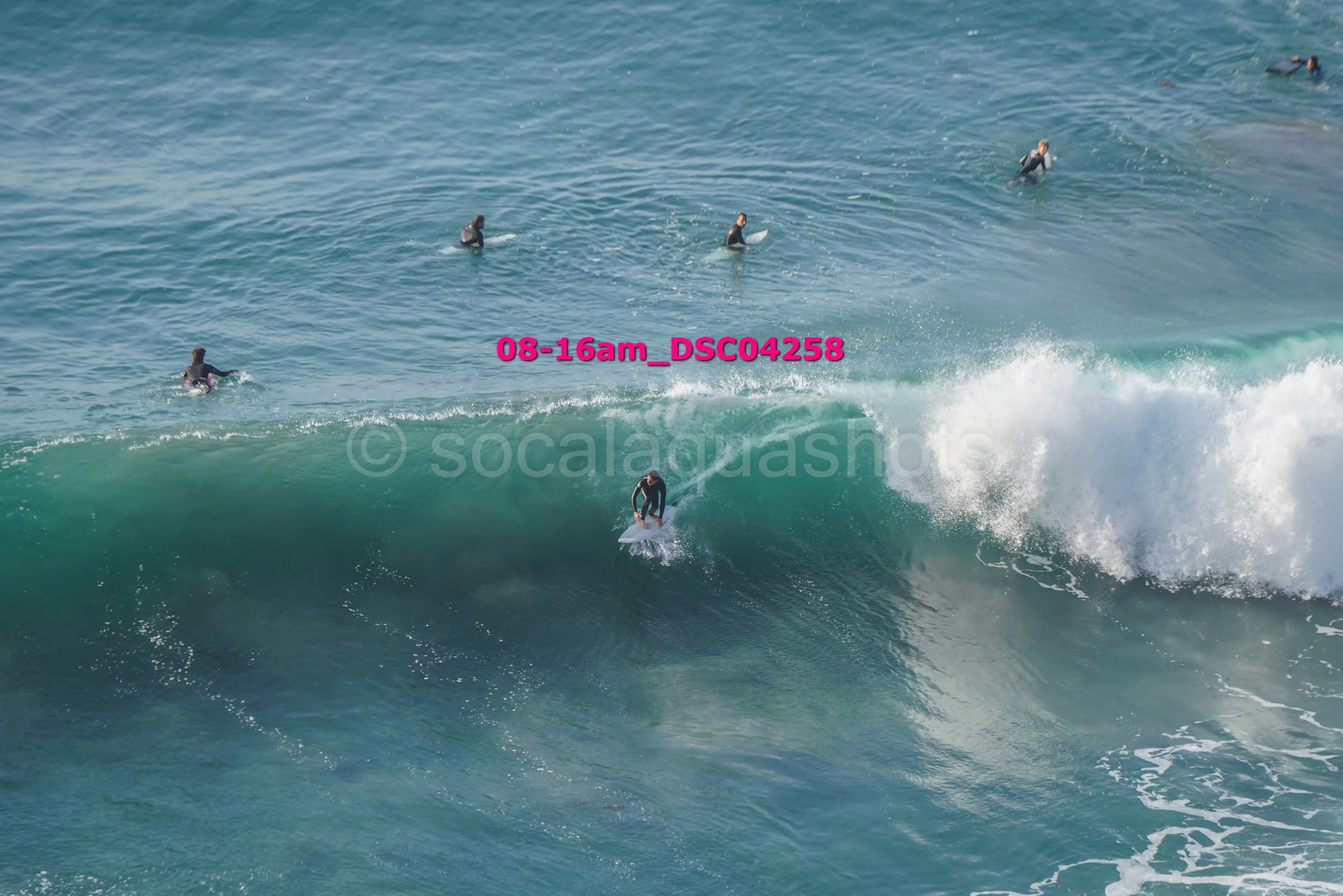 Surfer riding a wave with multiple people in the water in the background.