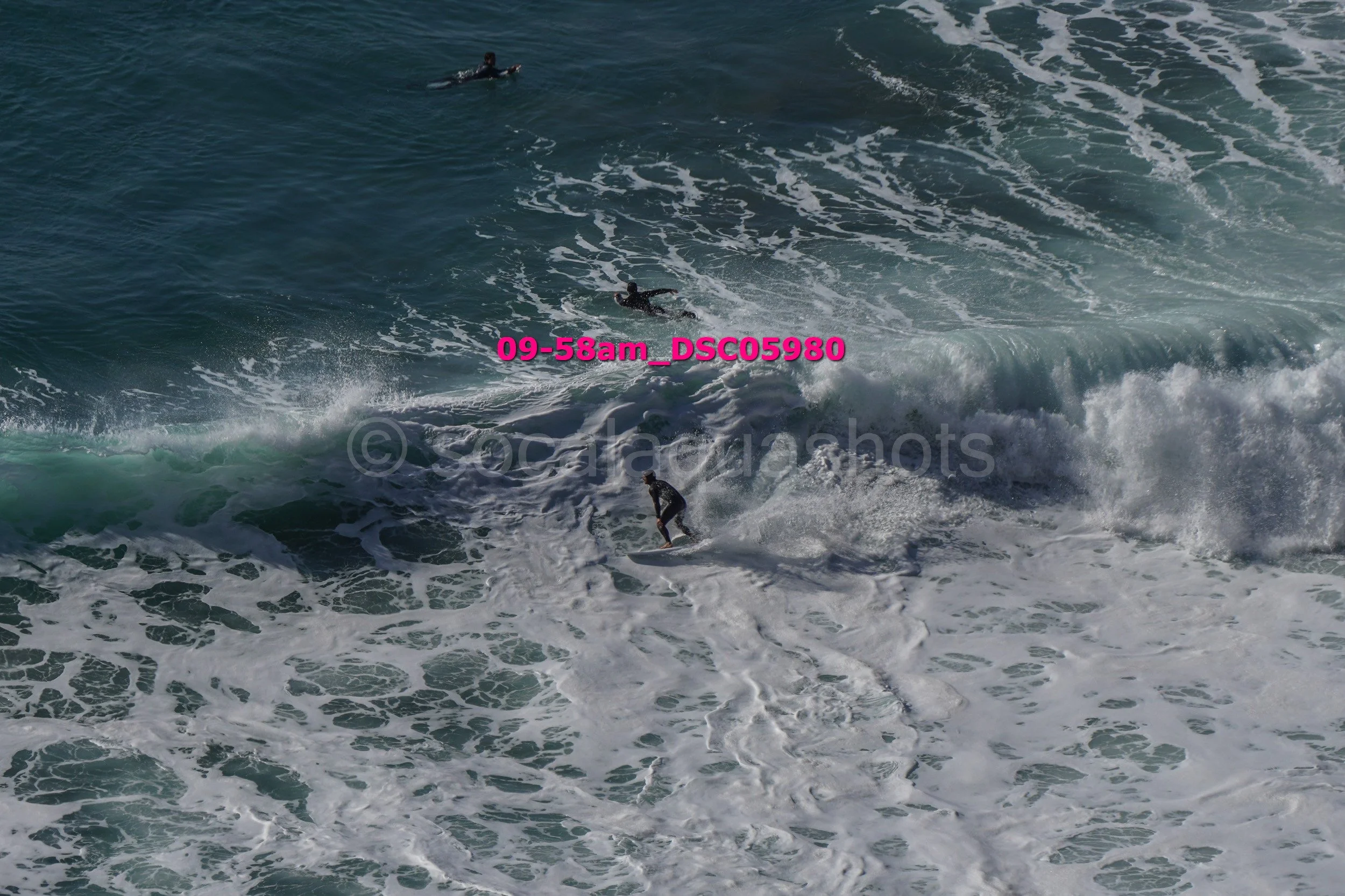 Several surfers riding ocean waves with white foam, viewed from above.