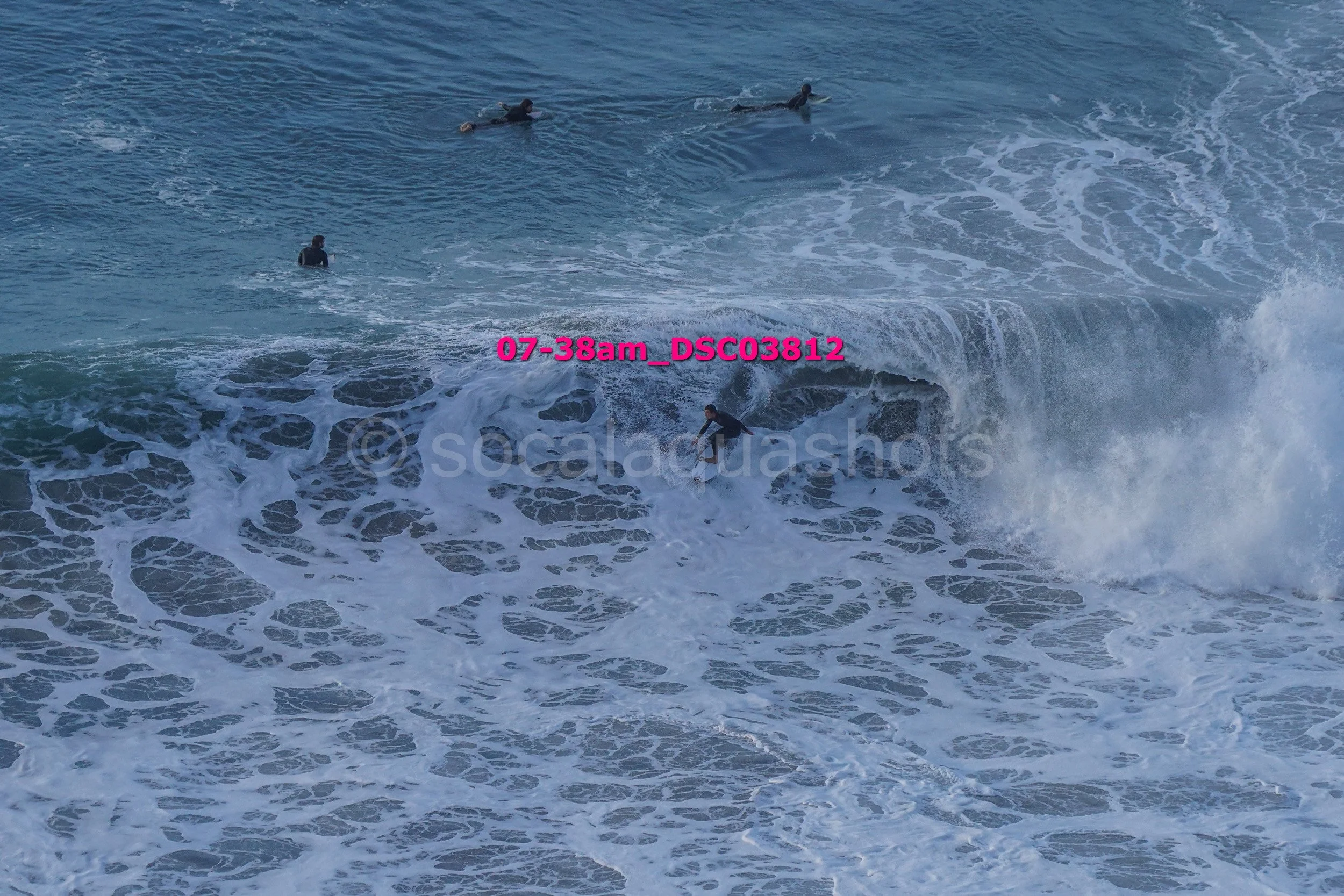 Surfer riding a wave with several swimmers in the water nearby.