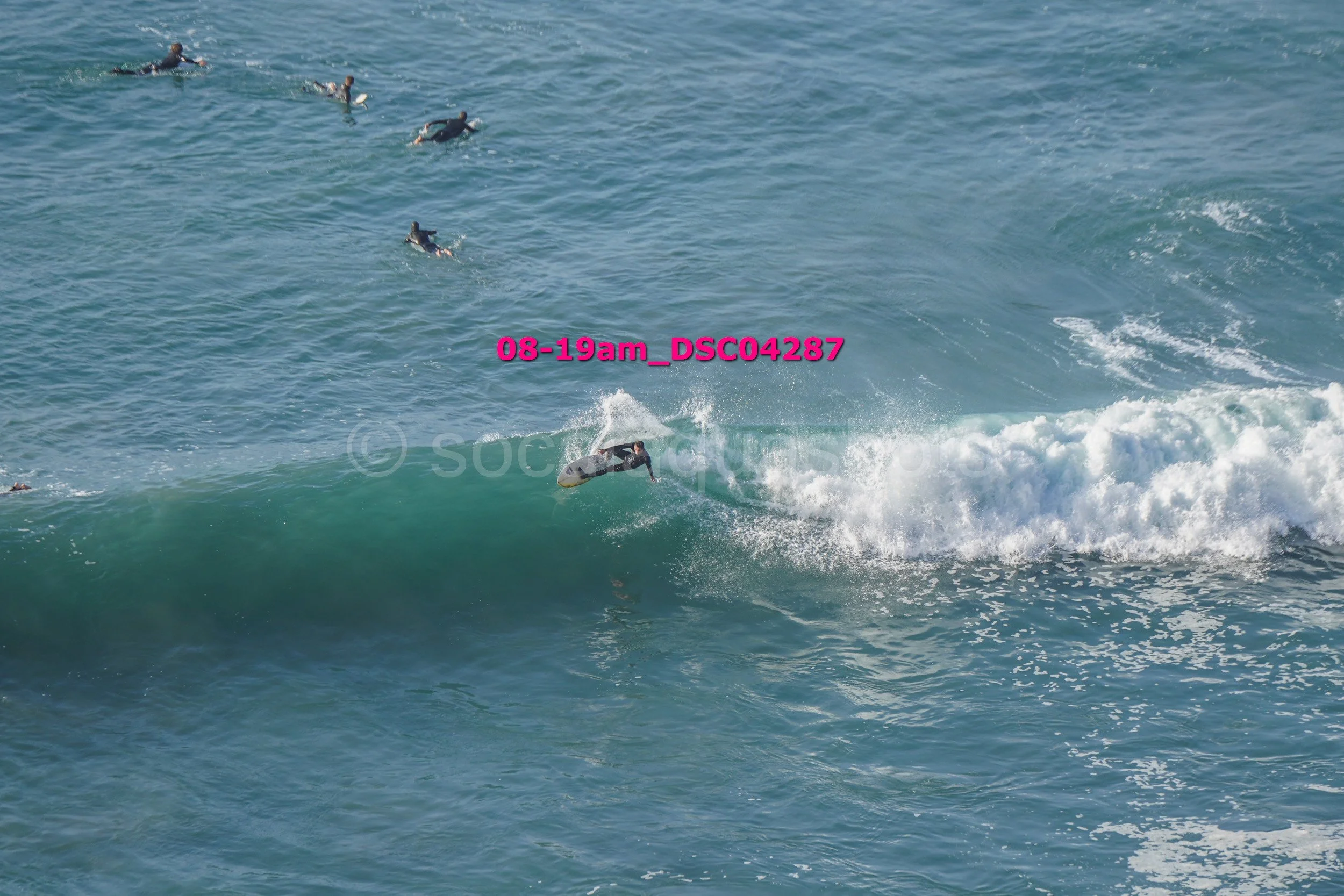 Person surfing on a wave with several others in the water nearby